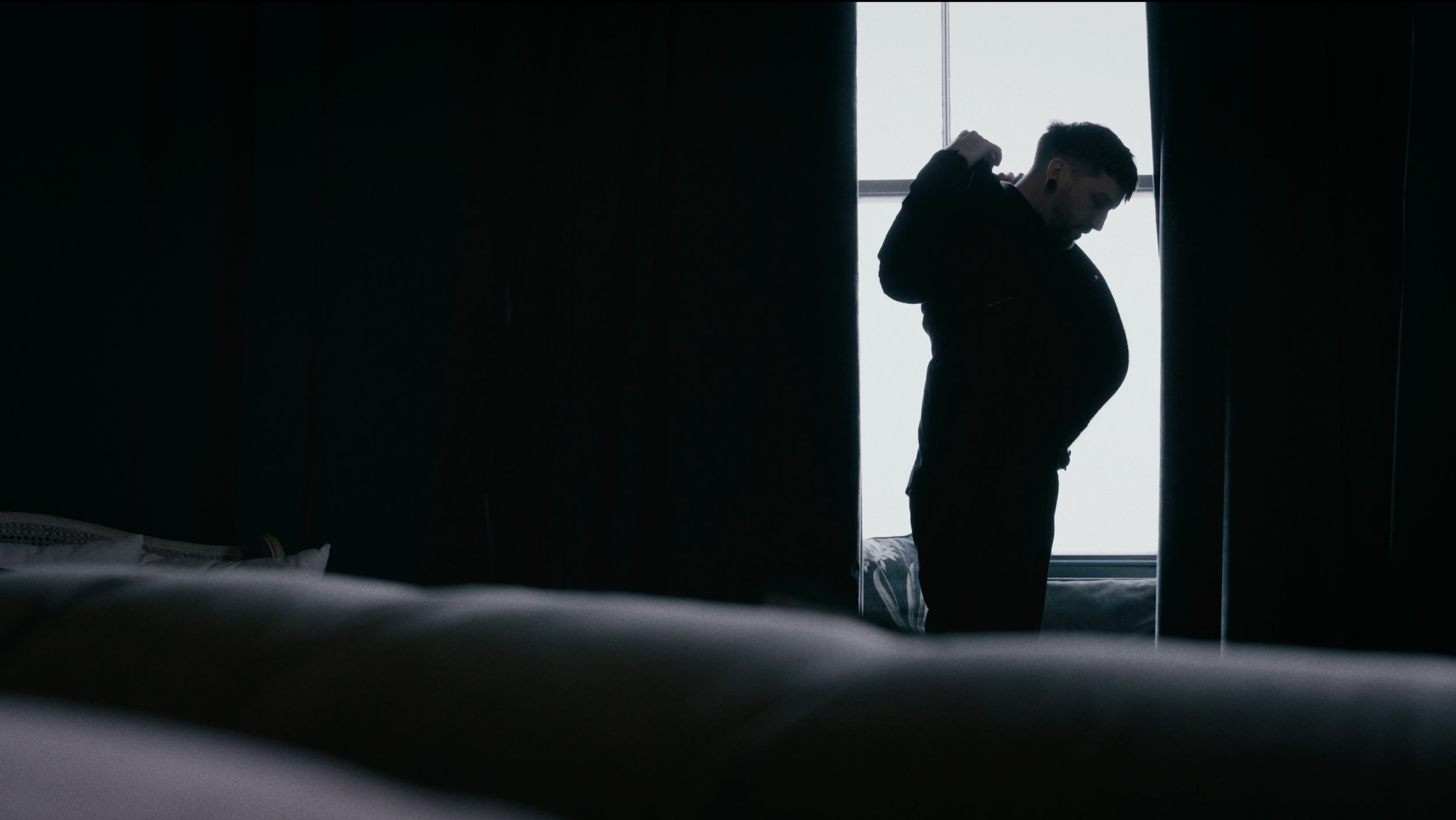 groom getting ready by a window in a dark room