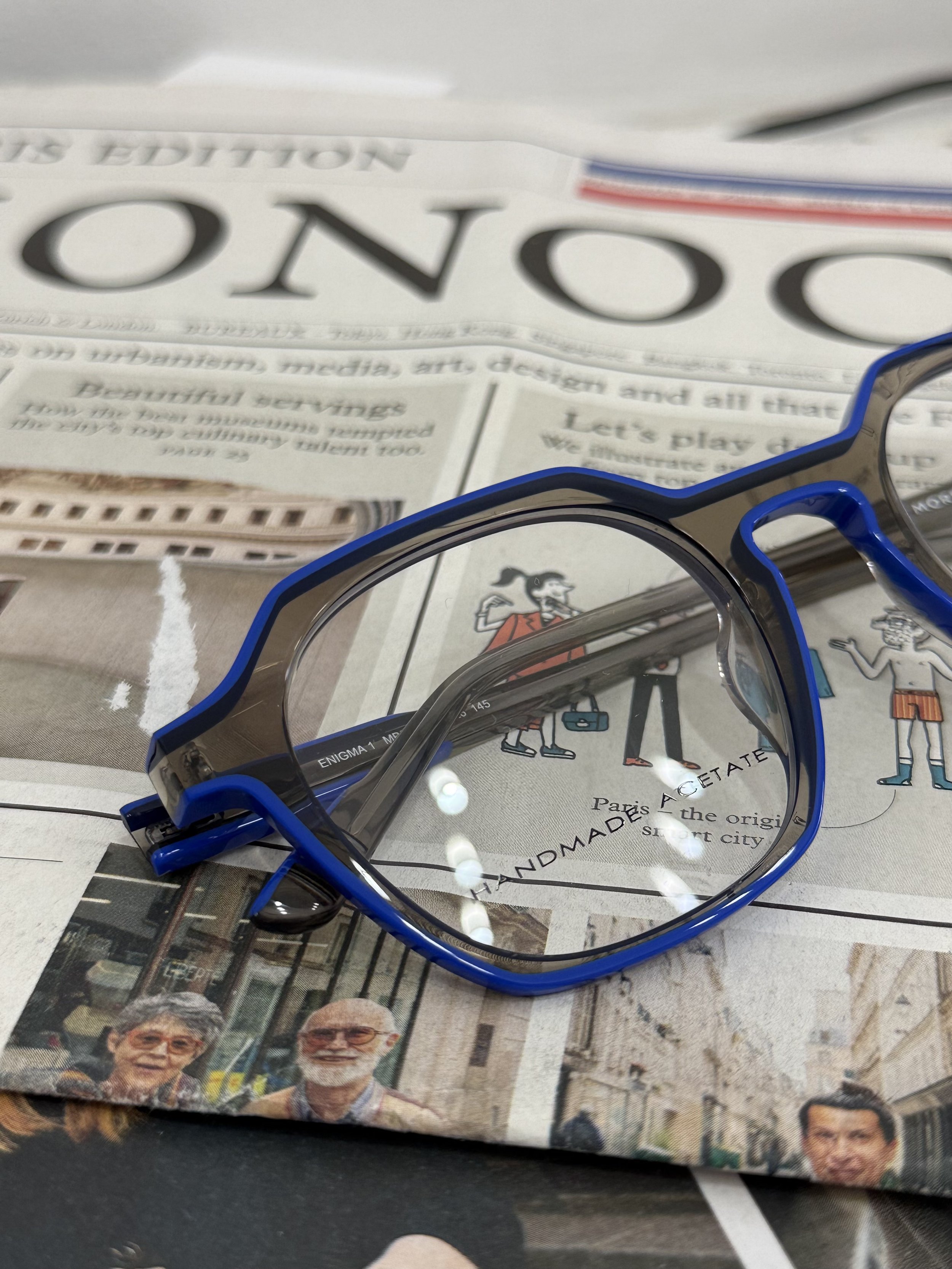 A pair of sports sunglasses resting on a newspaper with partial text and images, including a cartoon character and photographs of elderly people.