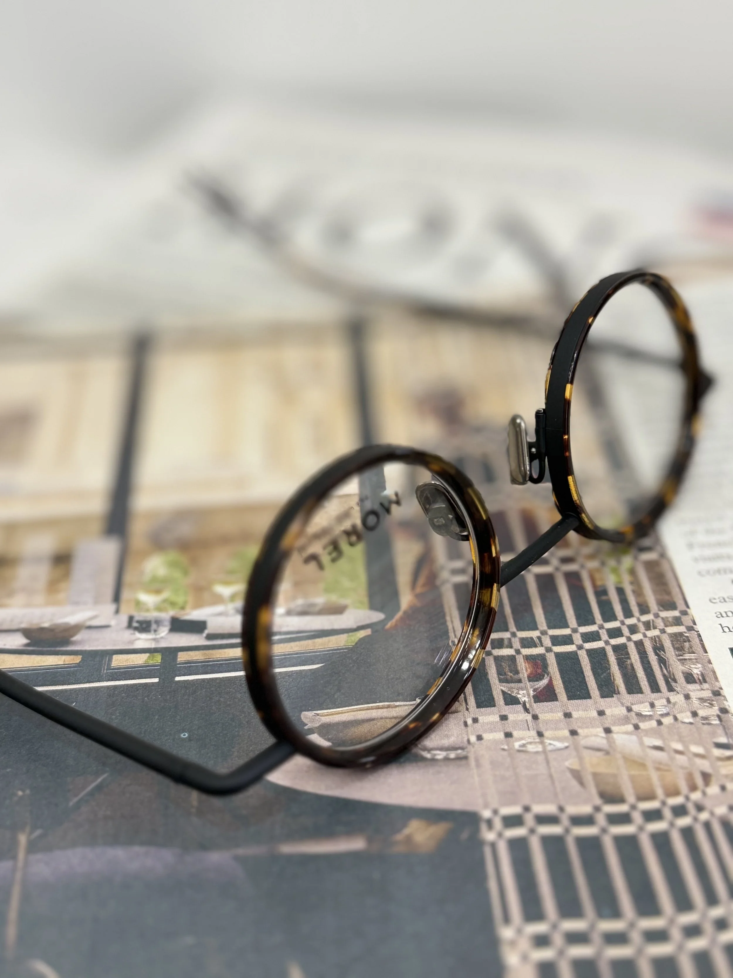 Tortoiseshell round eyeglasses resting on a magazine with architectural images, with a blurred white object in the background.