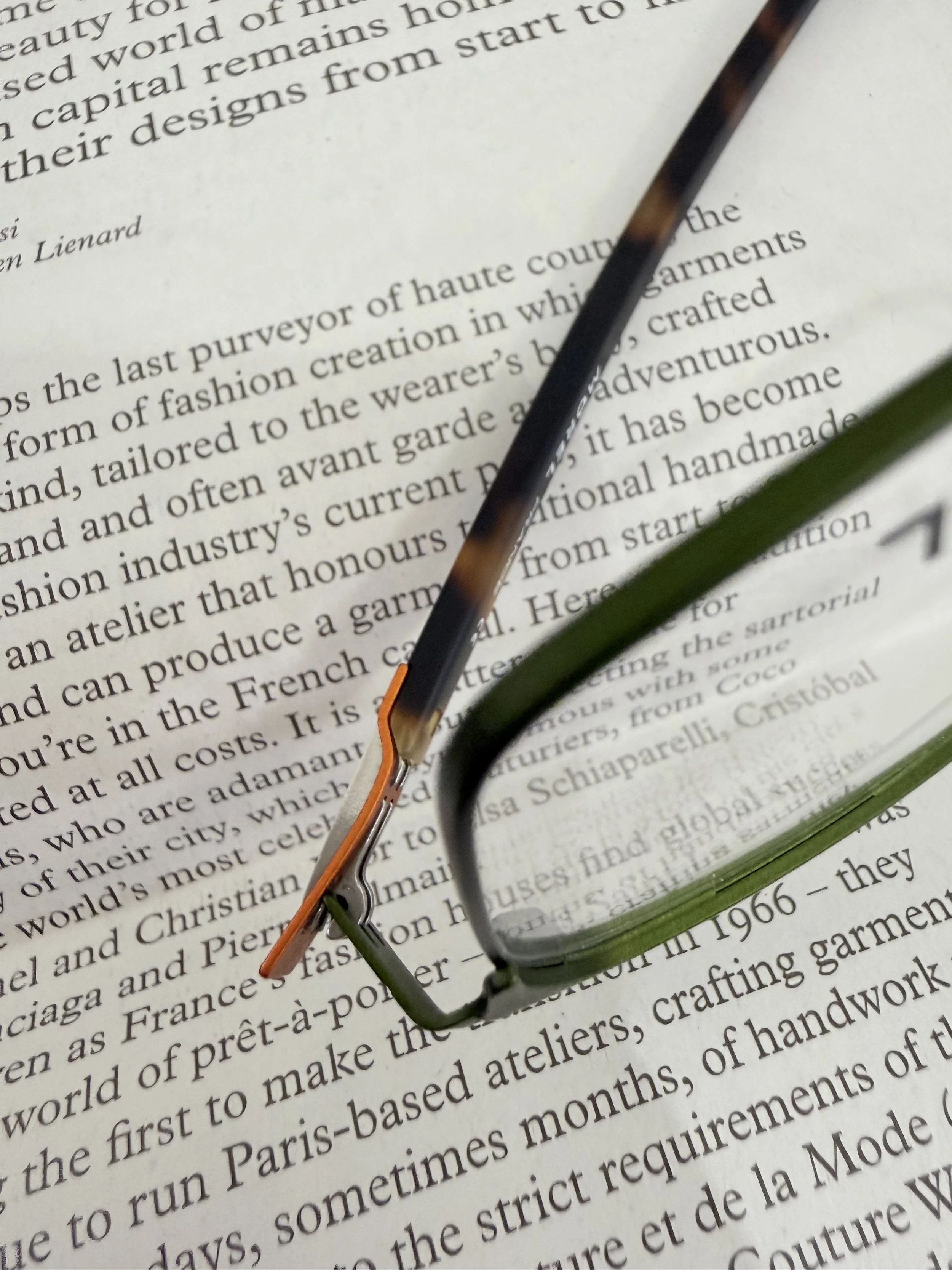 Close-up of eyeglasses resting on a page of printed text in a book or magazine. Morel szemüvegkeret a Showroom Optikában Budapesten.