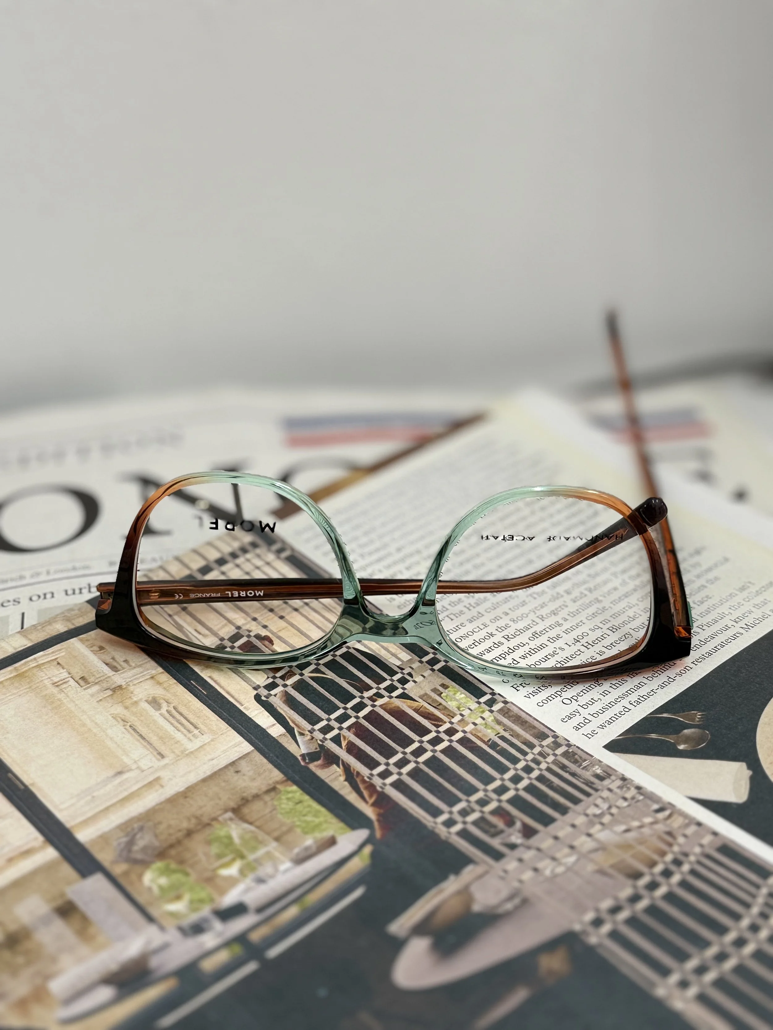 A pair of eyeglasses resting on an open magazine or book with pictures and text. Morel szemüvegkeret a Showroom Optikában Budapesten.
