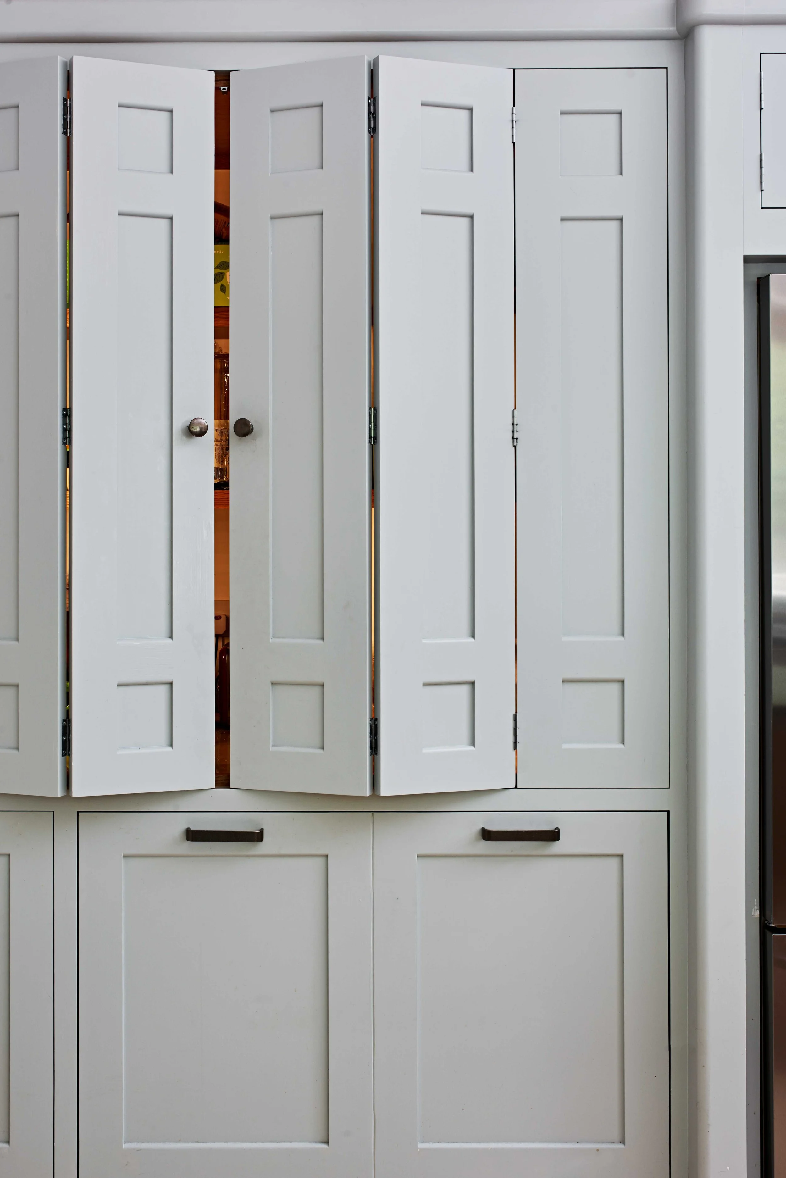 Soft grey handmade bifold cabinet doors slightly open in Surrey kitchen.