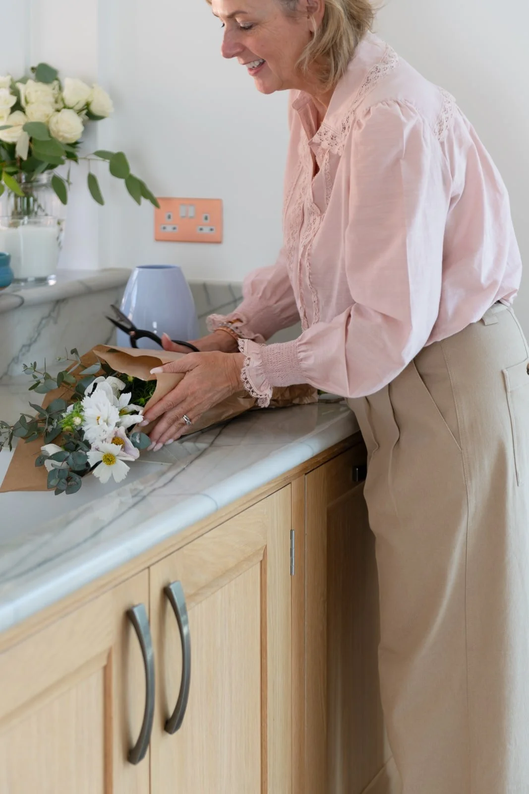 Karin Slater arranging flowers on handmade marble-topped sink unit in Surrey home.