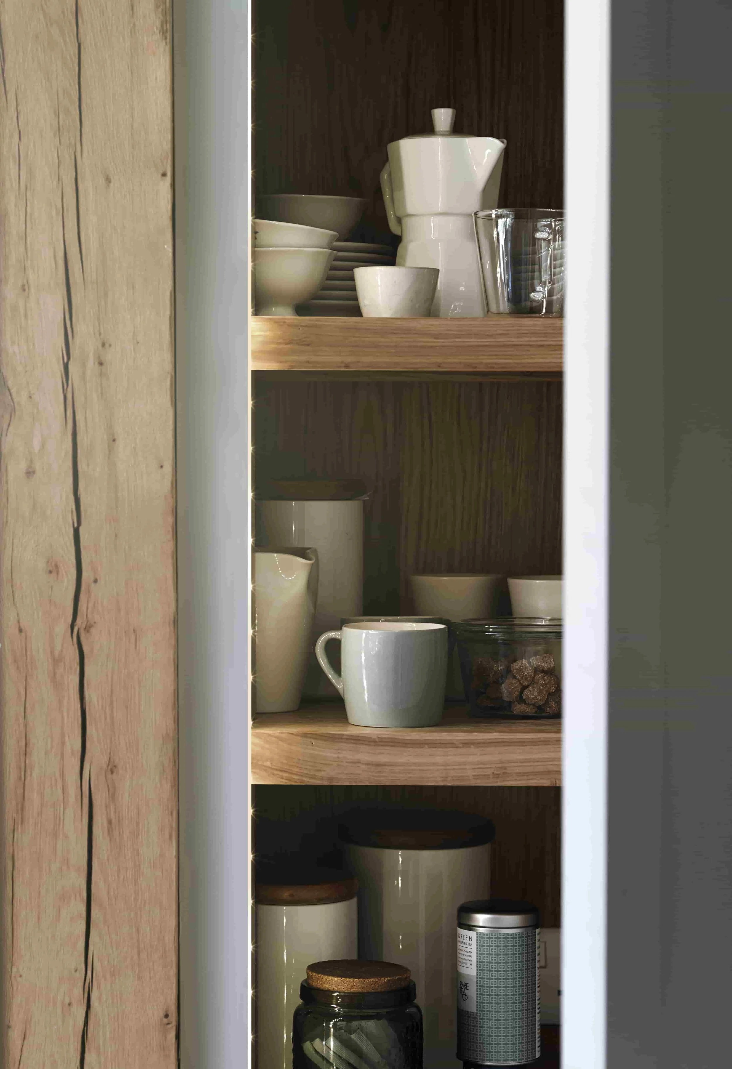 Tall bespoke larder cabinet positioned between original oak beams in handcrafted kitchen.