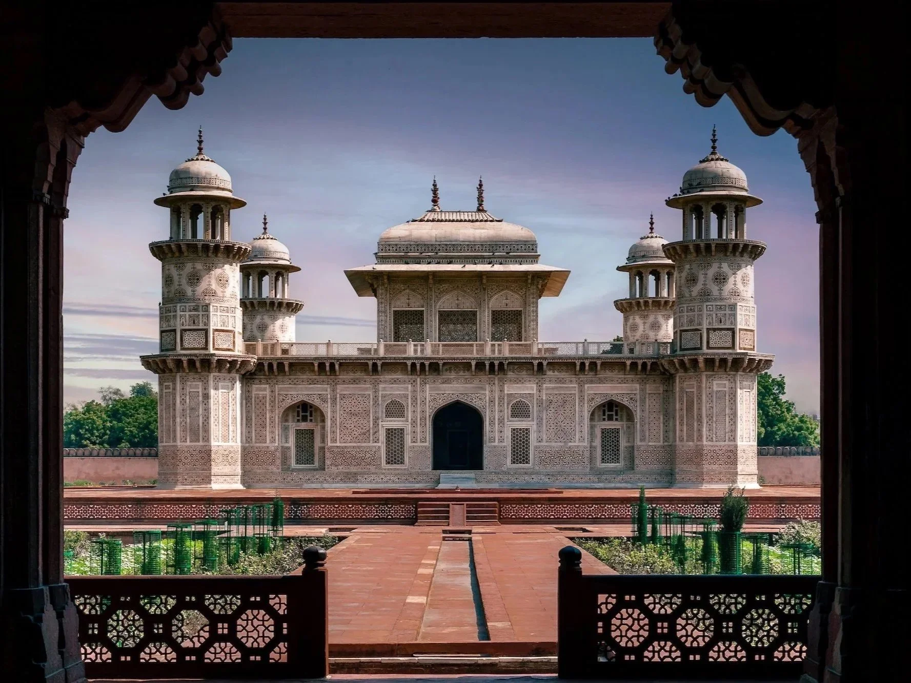 View of a historic white marble building with ornate architecture, four turrets, and a central dome, framed by a carved wooden archway.