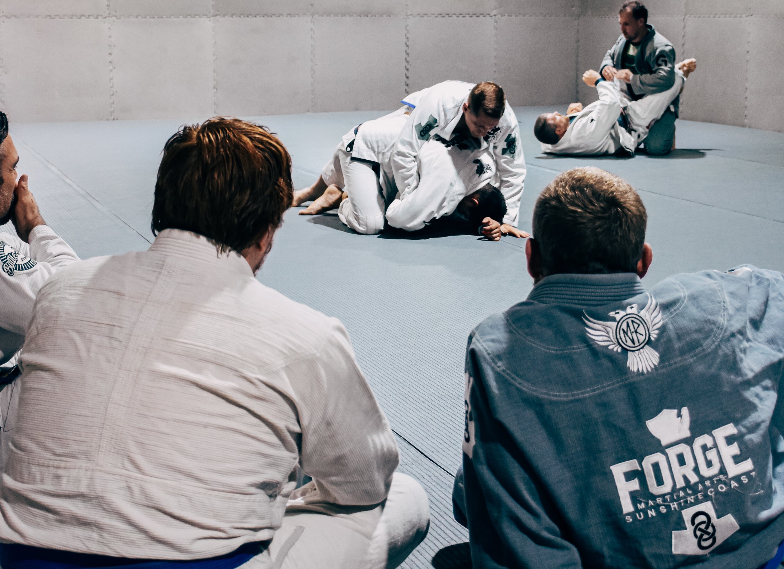 An over the shoulder shot of Coach Geordie and Big Matt watching Coach Chris rolling with Riley as he was grading for his blue belt. Coach Nate and Adam also rolling in the background.