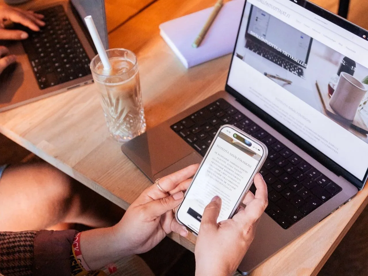 Henkilö selaa sisältöä puhelimelta kahvilan pöydän ääressä.