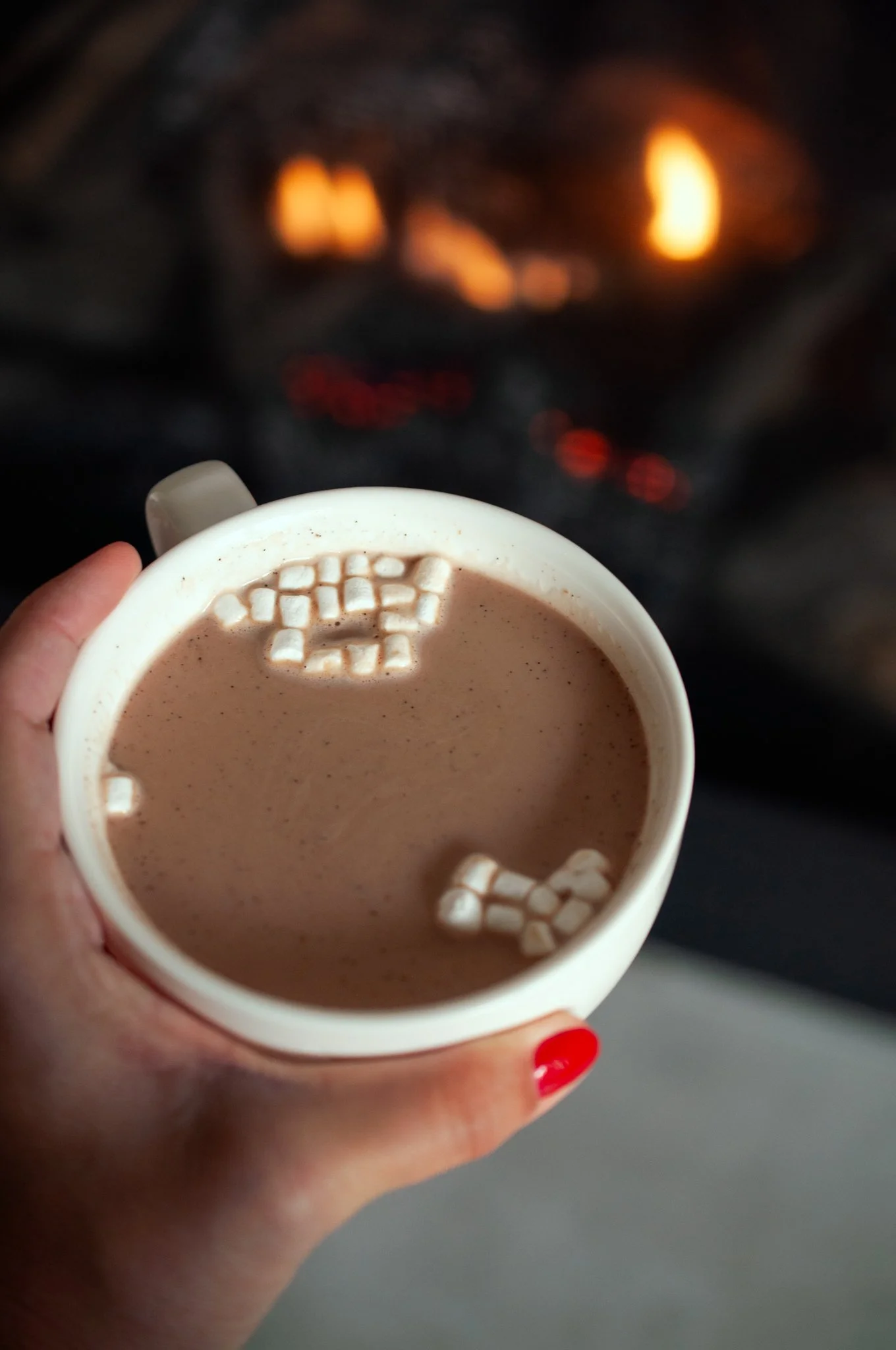 mug of hot chocolate and mini marshmallows near a fire