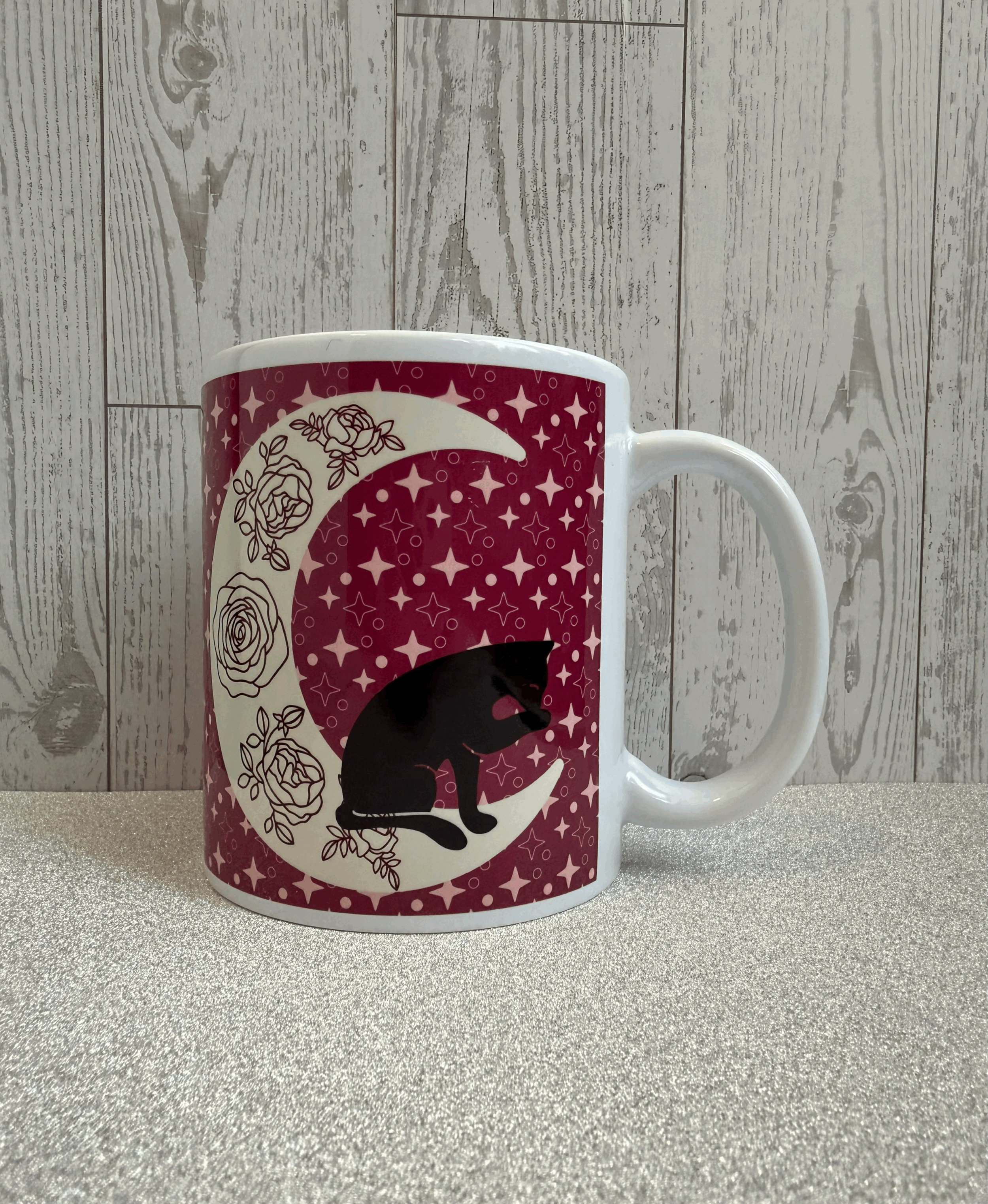 Summer themed black cat and moon mug featuring a black cat licking it's paw while sitting on a crescent moon adorned with roses.gif