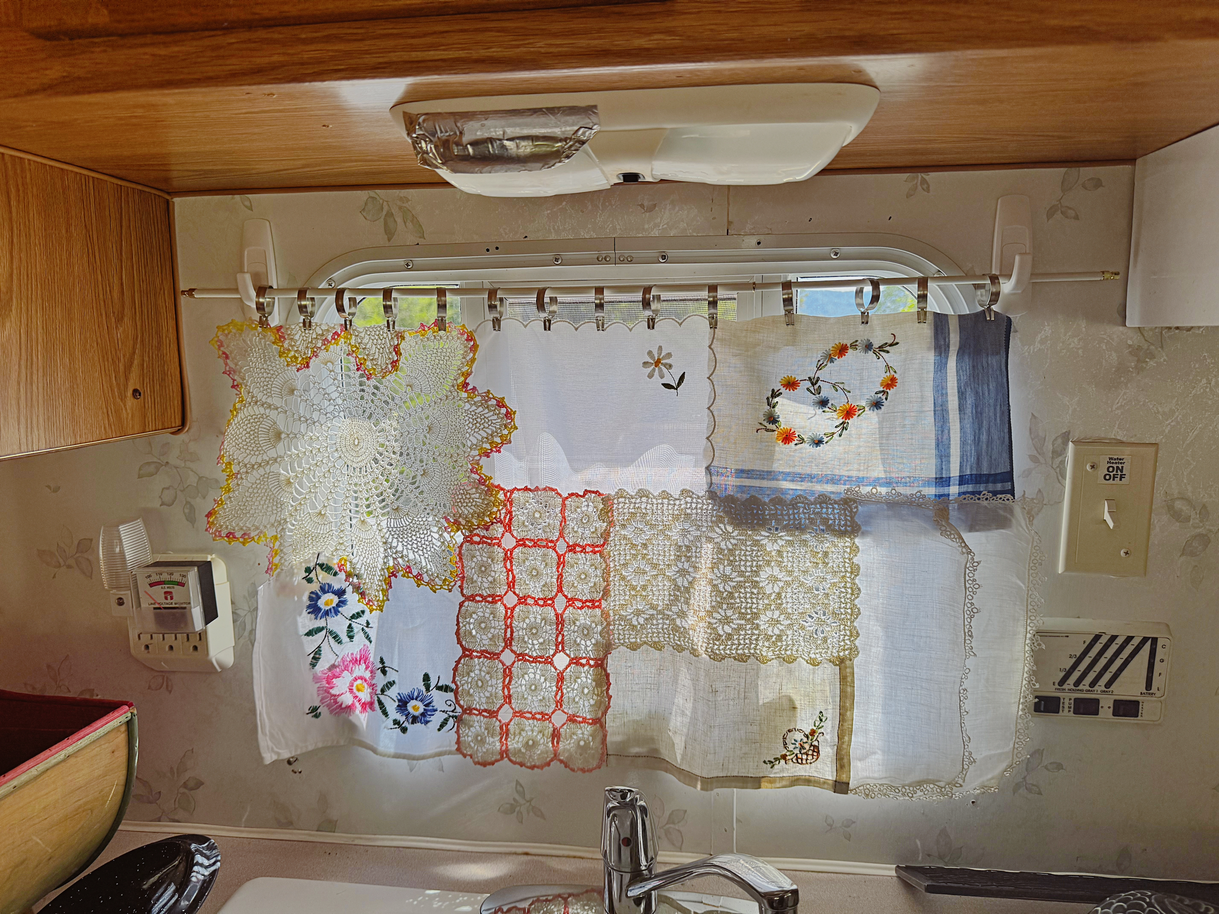 A small curtain made from scraps of table cloths, doilies, and cloth napkins hanging in a camper window.