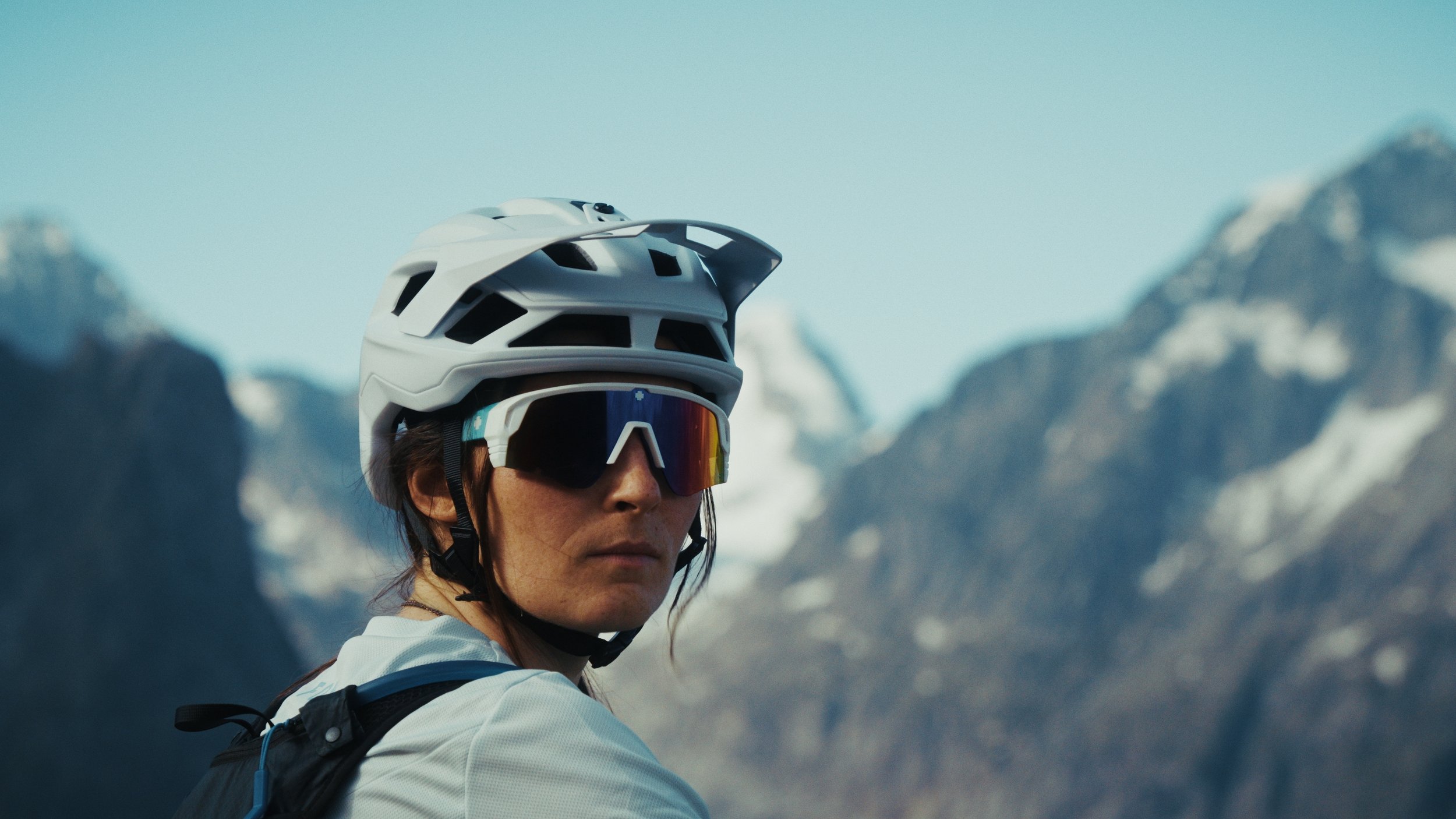 Etalonnage de Kevin Rocha. Femme portant un casque de vélo, lunettes et un sac à dos, avec des montagnes en arrière-plan.