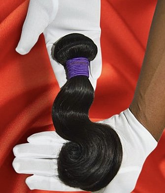 A bundle of black hair with purple and black bands, being held with white-gloved hands against a red background.
