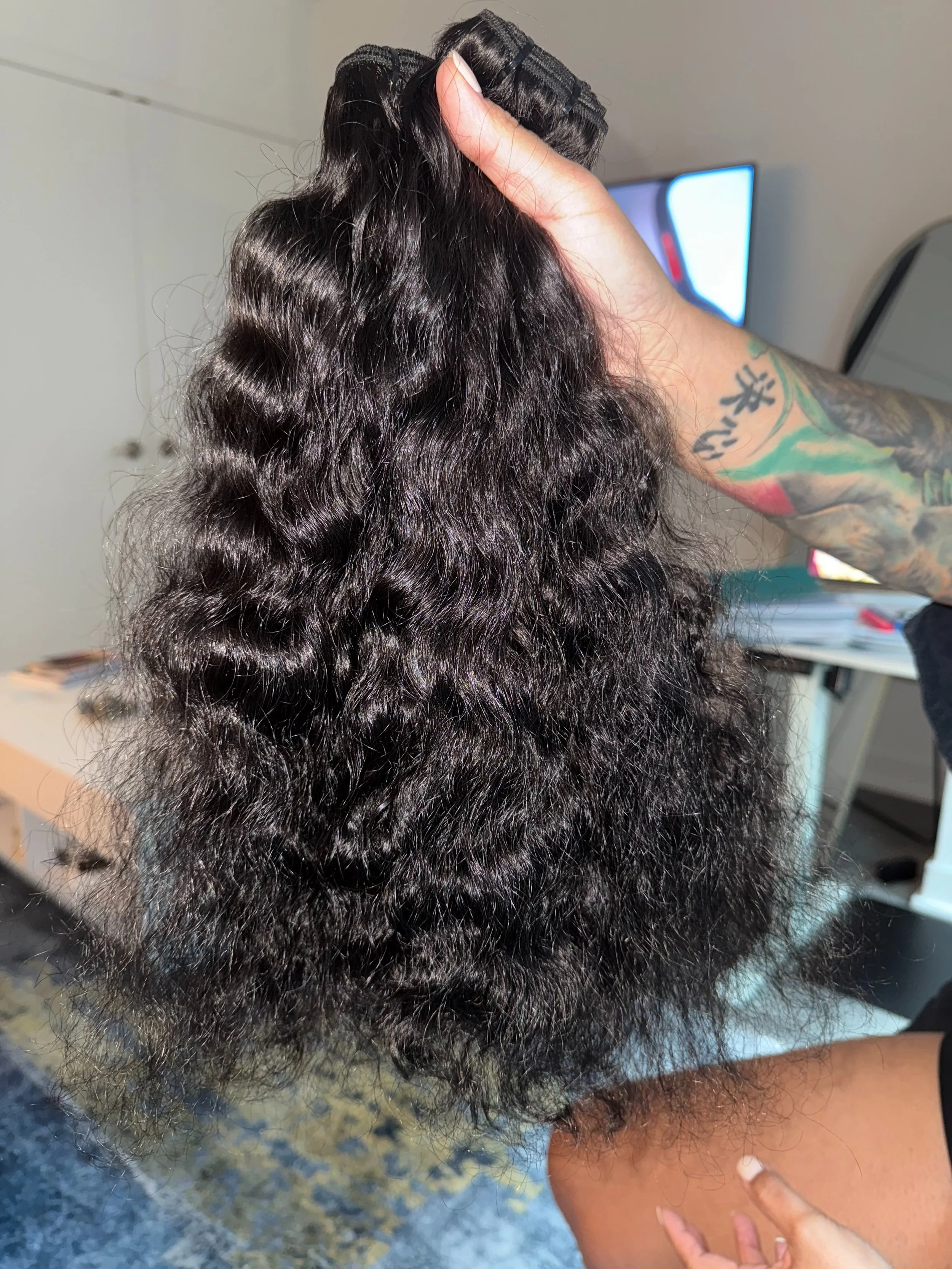 Close-up of a person holding a bundle of wavy, black hair extensions or natural hair.
