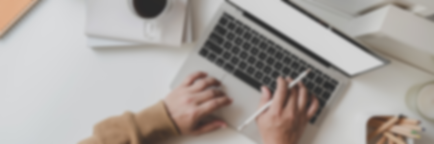 Person typing on a laptop with a stylus pen in a bright workspace.