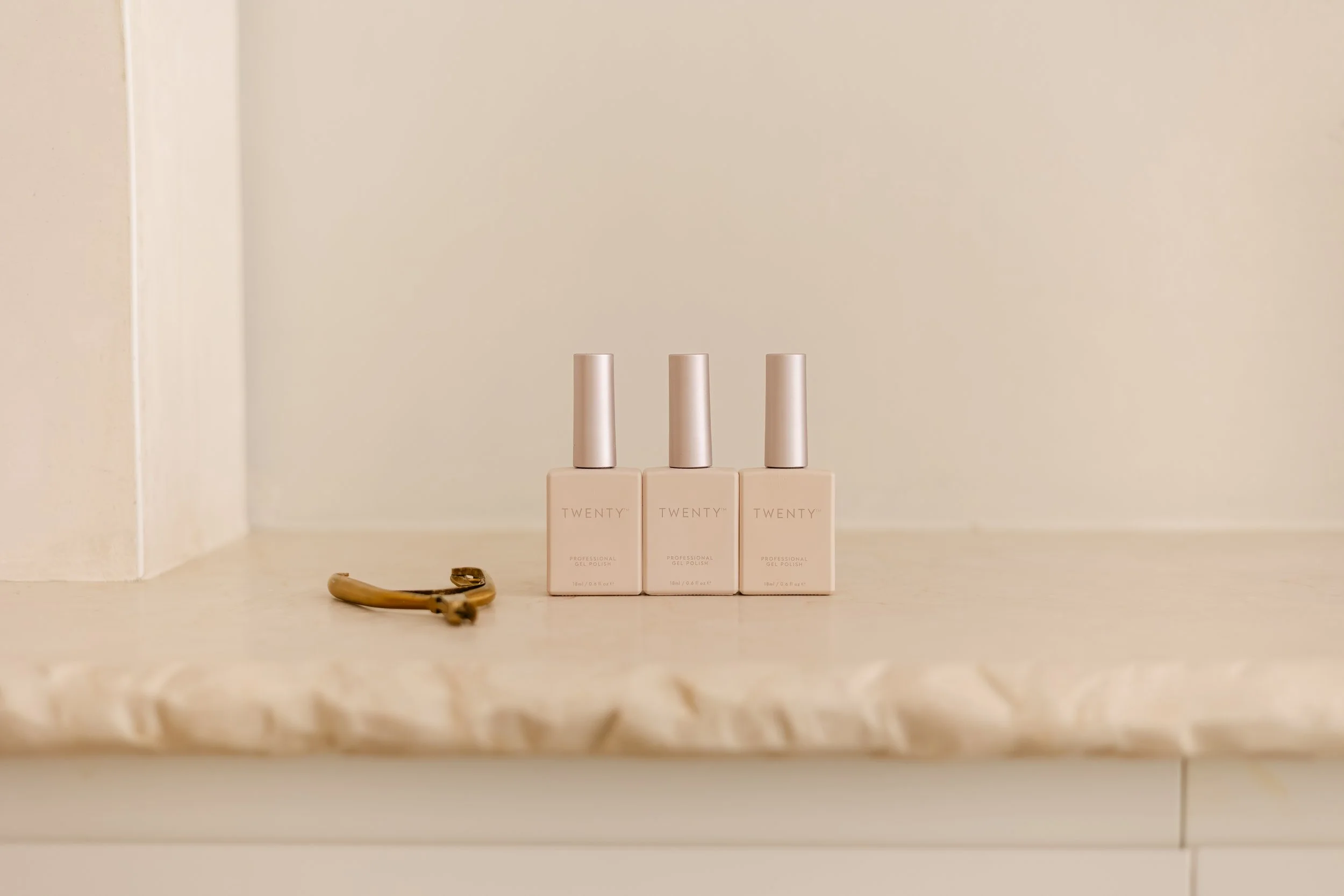 Three bottles of professional gel nail polish and a tortoise shell hair clip on a marble countertop.