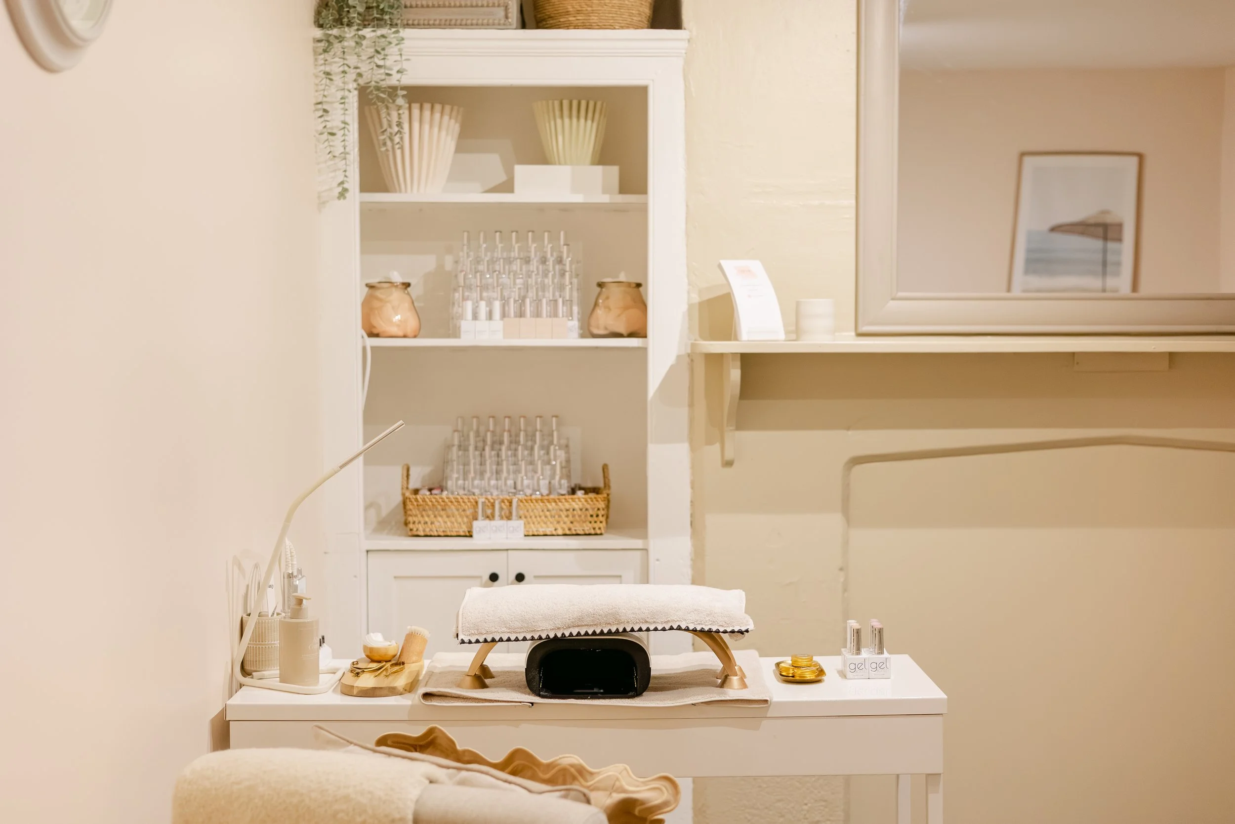 A massage or therapy room with a massage table covered with a towel, surrounded by skincare and wellness products, in a softly lit, calm environment with shelves displaying decorative items and skincare products, and a mirror on the wall.