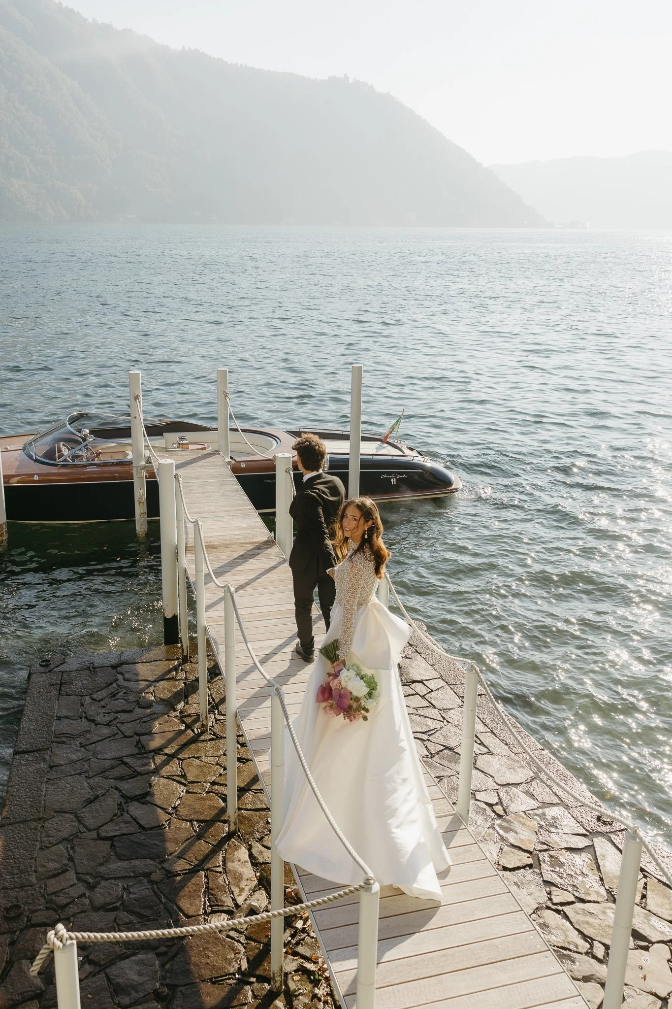 The couple is walking toward to the boat. The bride is looking over her shoulder.