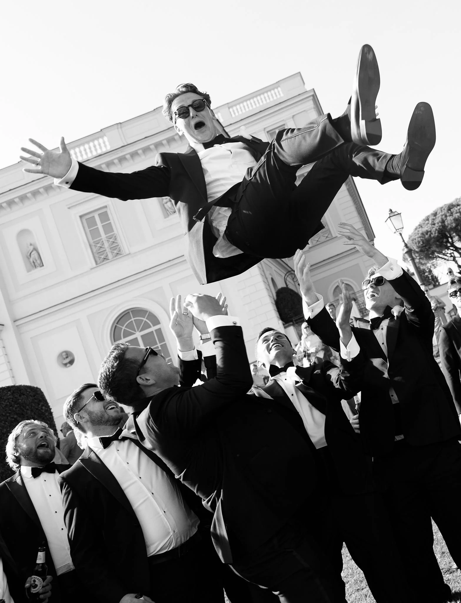 Grooms party boys are throw the groom up. All dressed in tuxedos.