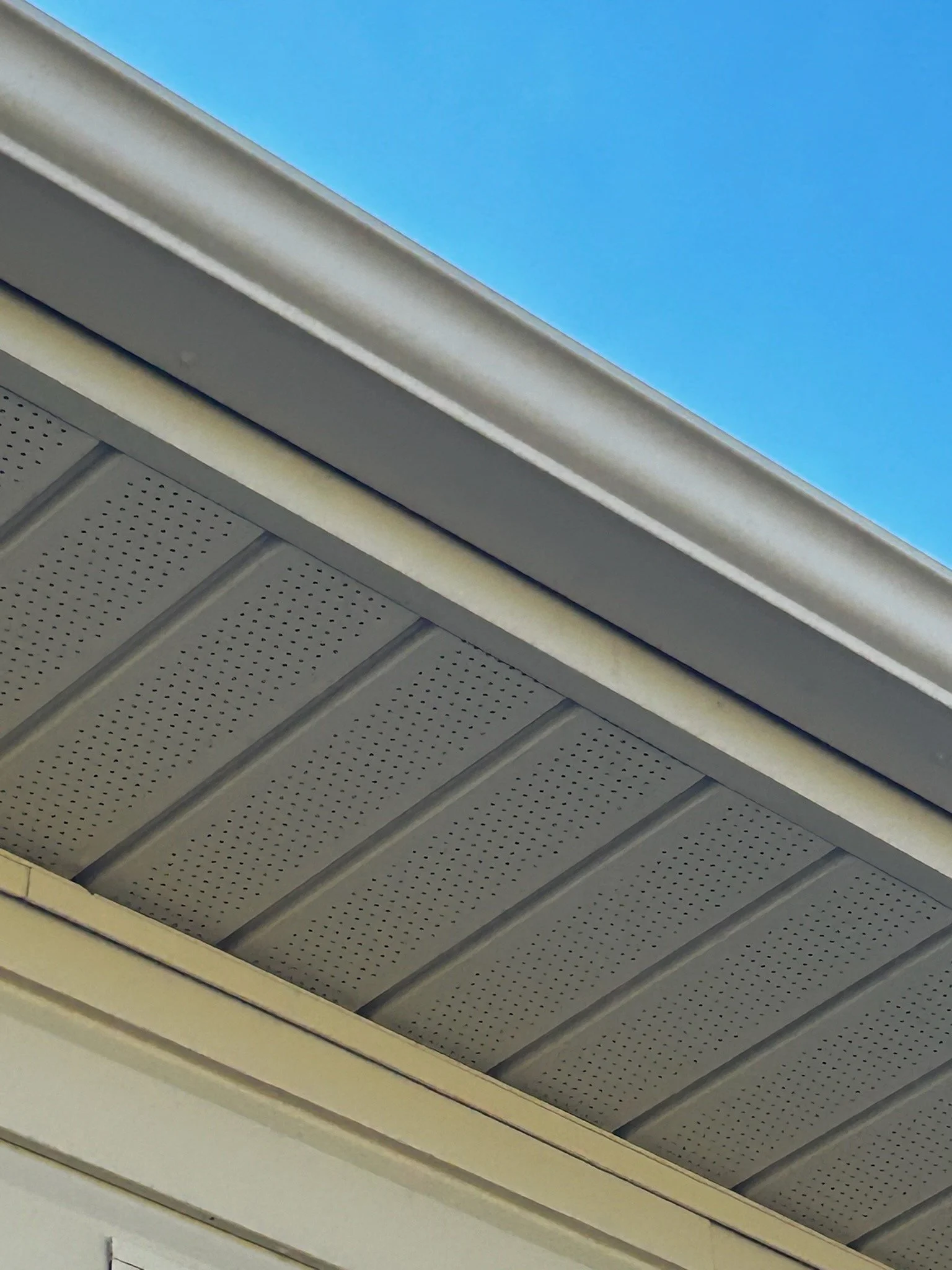 Close-up photograph of the underside of a house roof strap with blue sky in the background, showing details of the gutter and roof soffit.