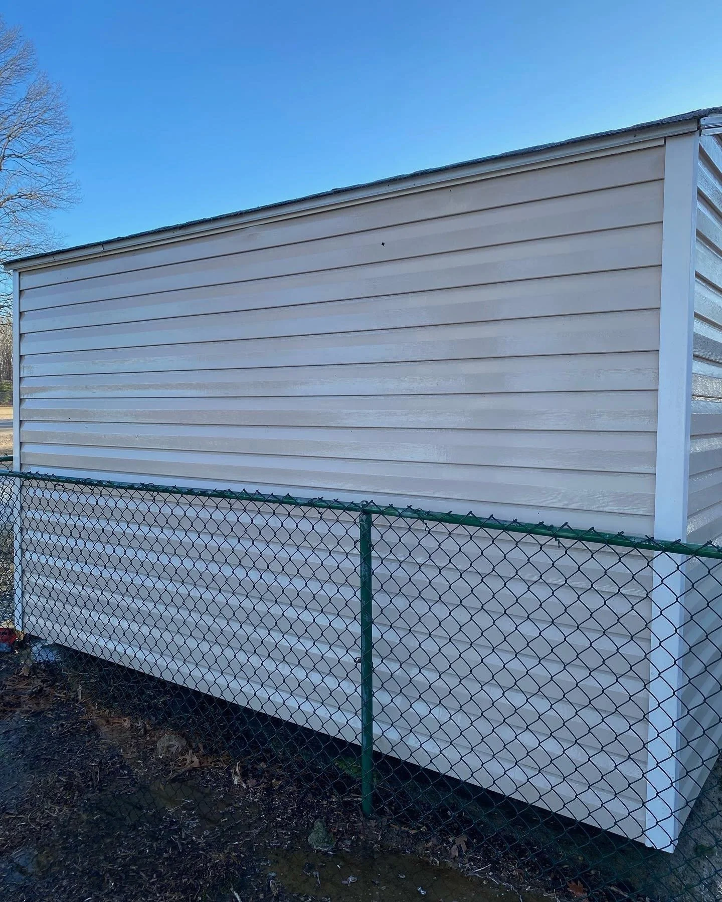 White storage shed with horizontal siding, surrounded by a green chain-link fence, under a clear blue sky.