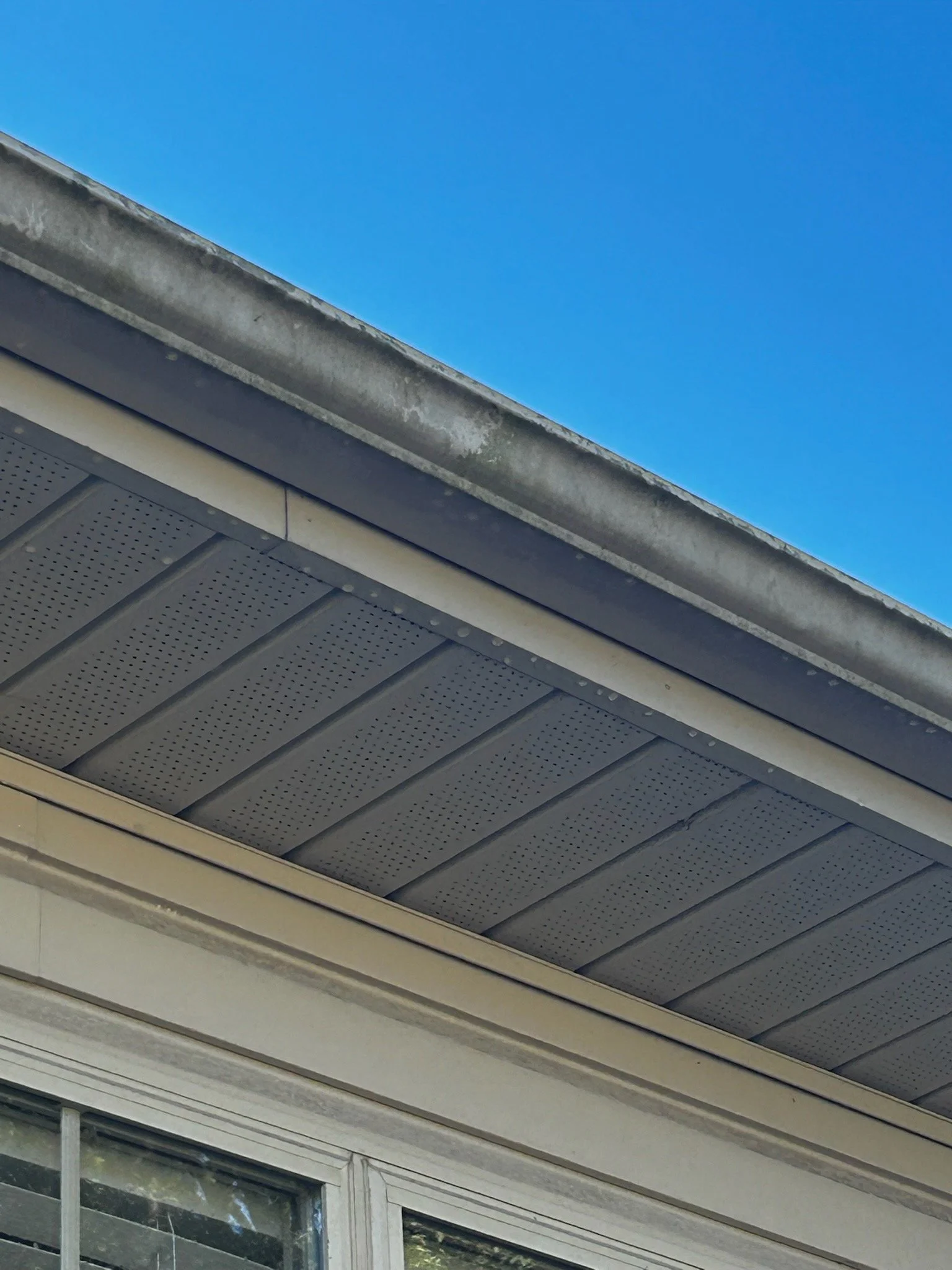 Close-up of a house's soffit and fascia with a gutter, under a clear blue sky.