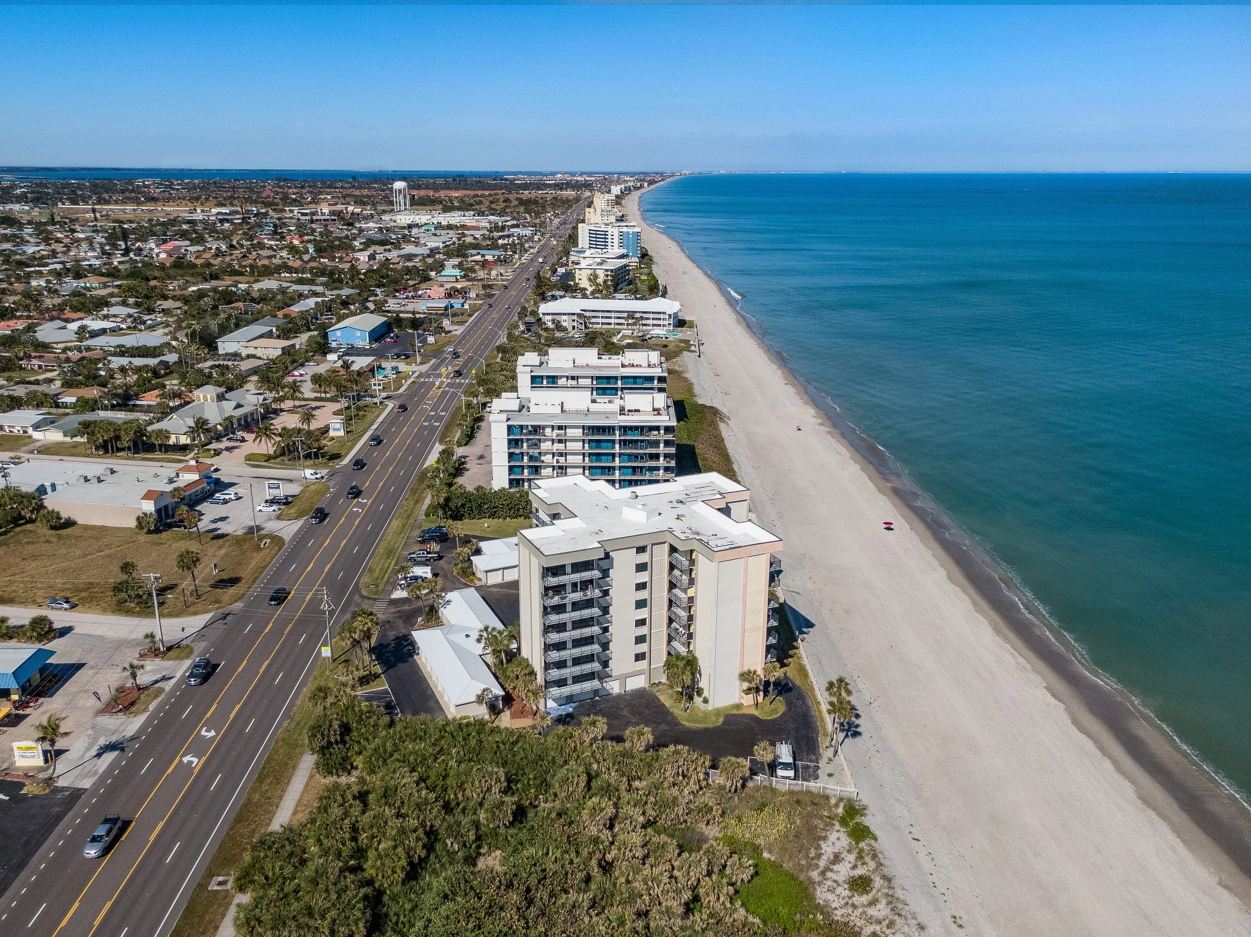 Aerial drone view of ocean front condo buildings between the beach and a highway.