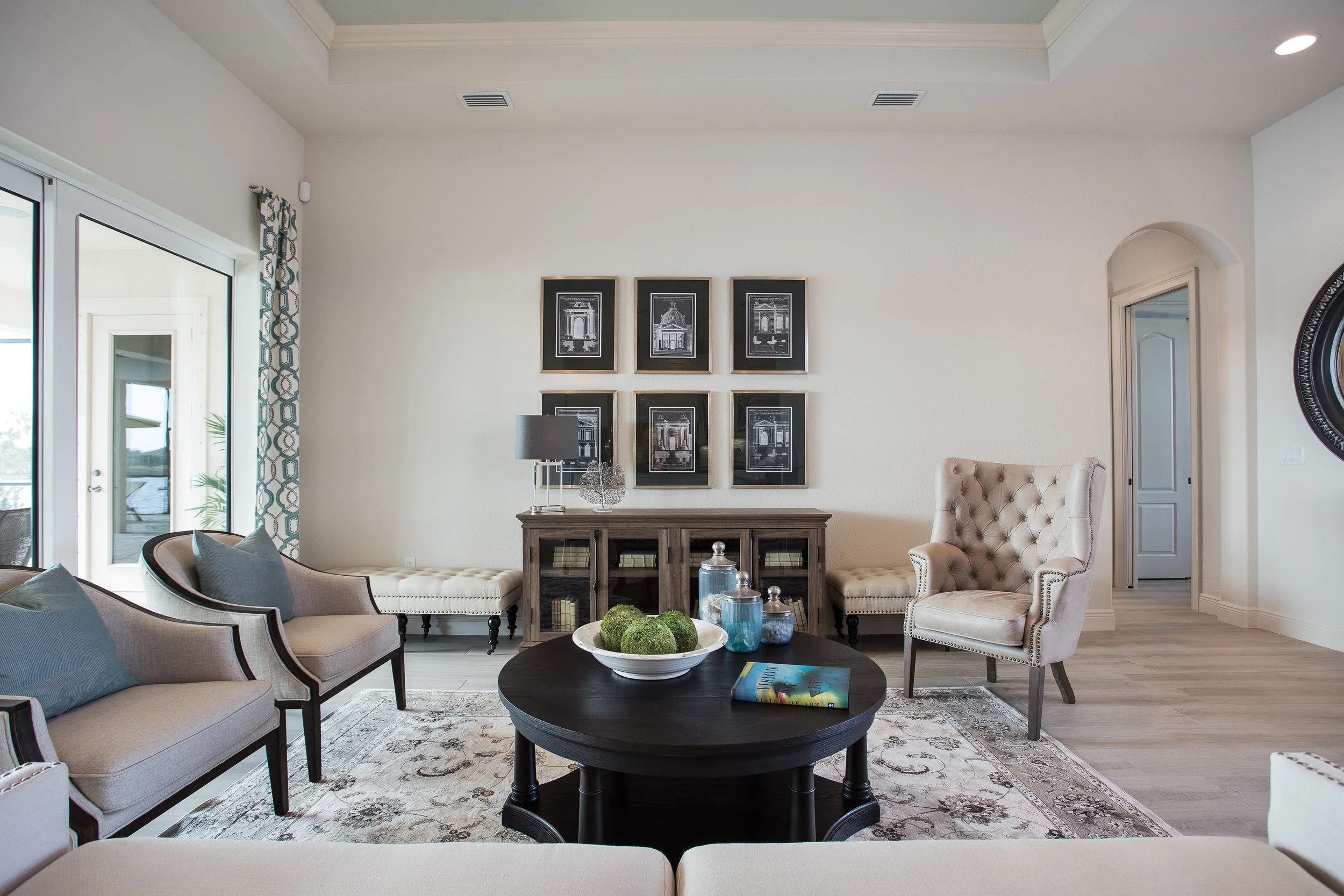 Living room with beige and grey furniture, black coffee table with book and decor, wall art, and sliding glass door.