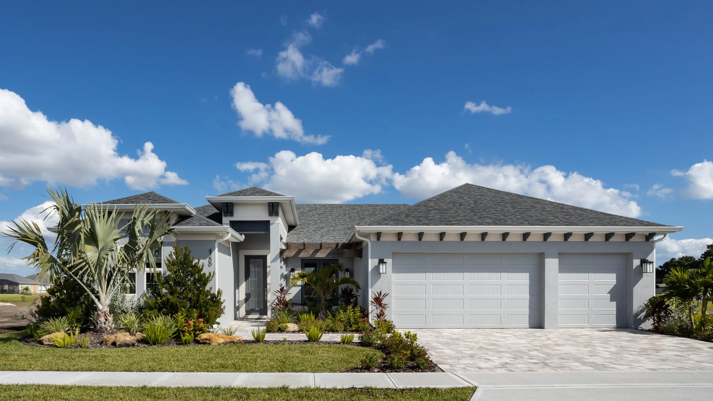 Front exterior of a light blue Florida home with tropical landscaping and blue sky.