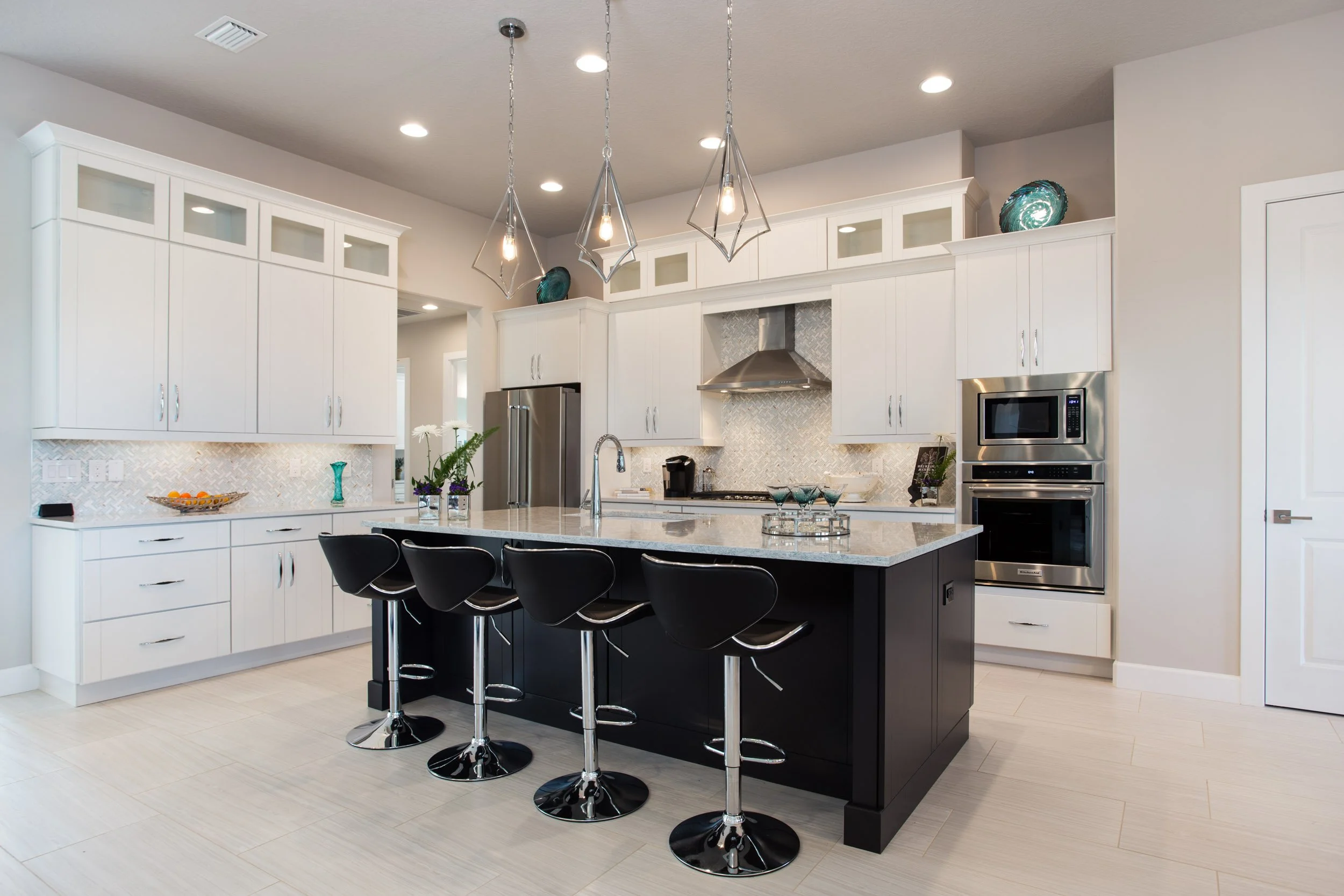 Modern kitchen with white cabinets, black island, stainless steel appliances, and pendant lighting.