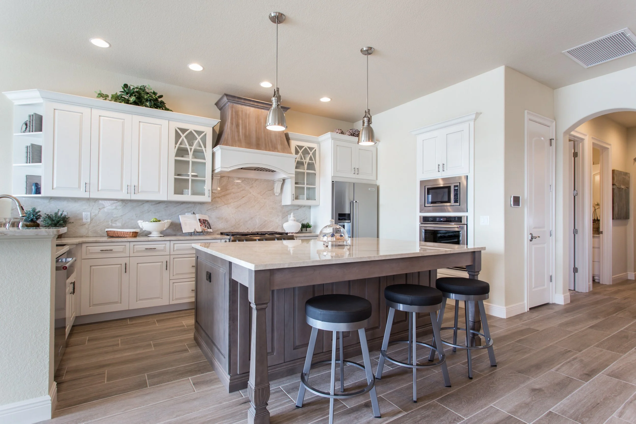 Modern kitchen with white cabinets, a marble backsplash, stainless steel appliances, a large island with a light-colored countertop, and three black stools