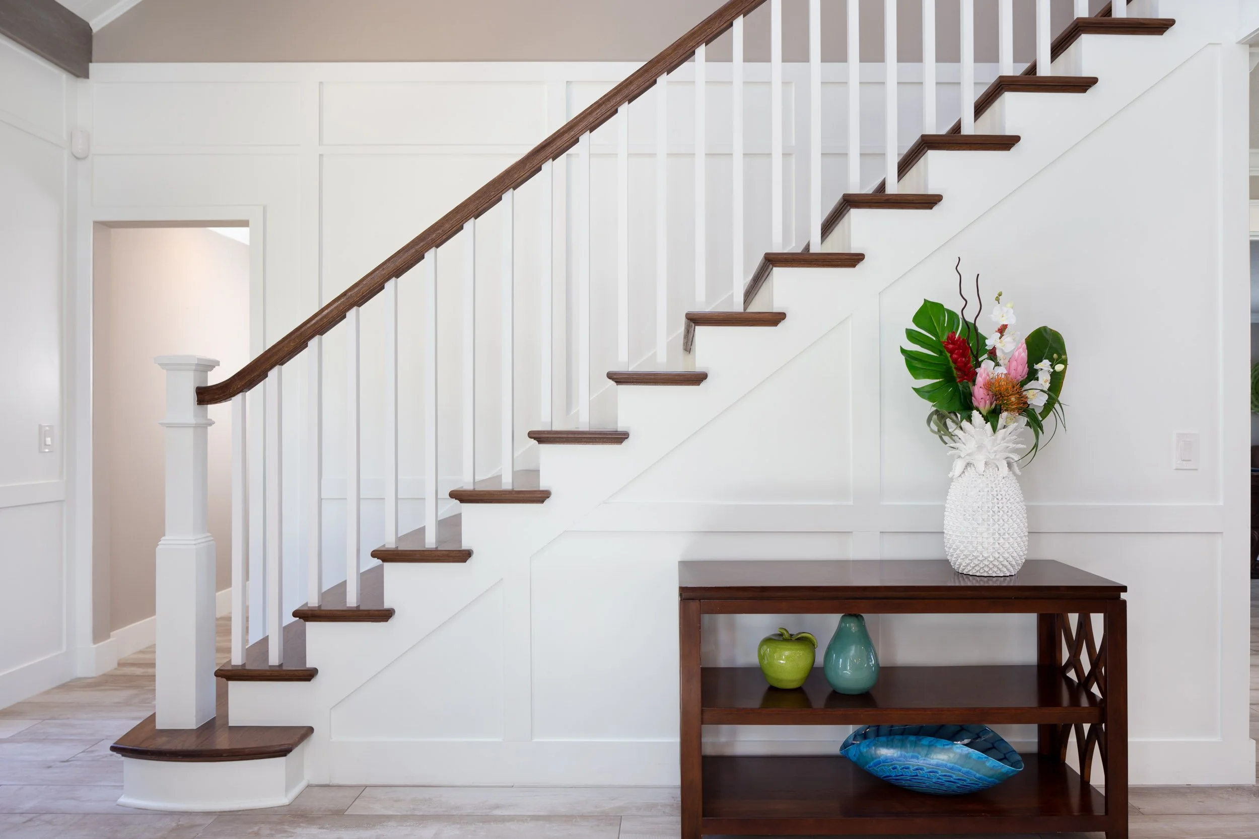 Side view of a wooden staircase with white walls and small shelf unit and colorful decorations