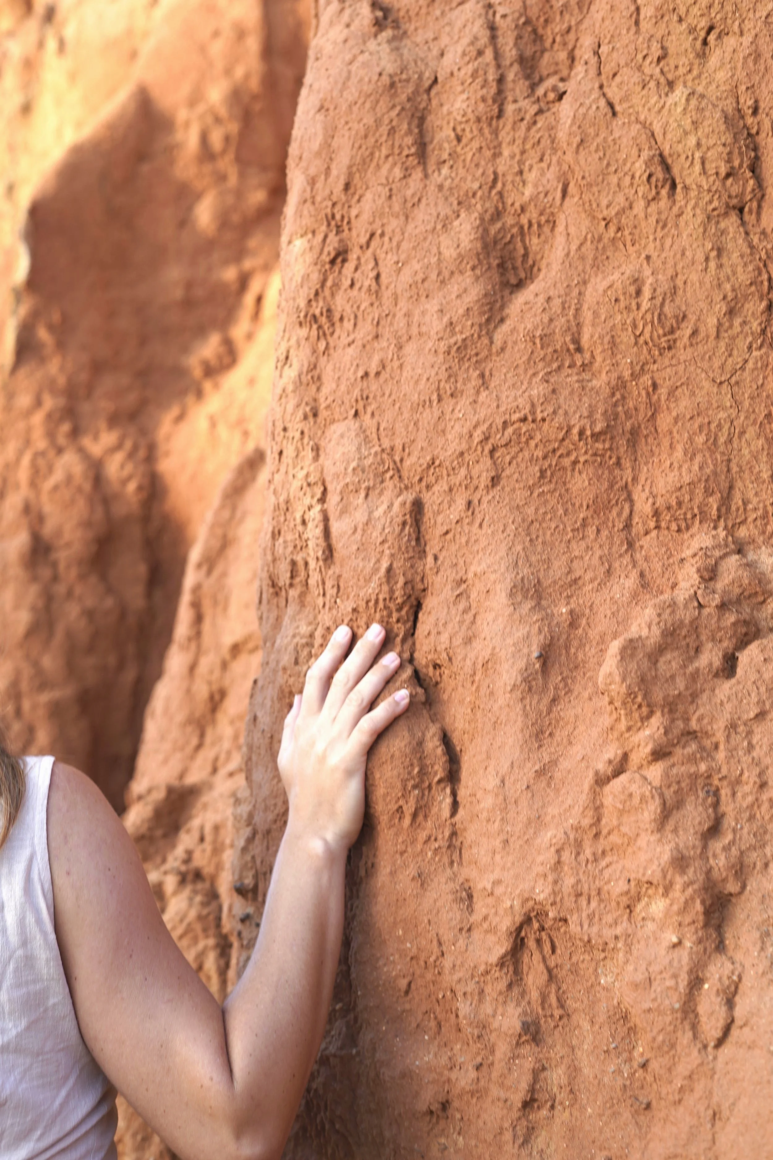Close-up of a person touching a rough, sandy red rock surface with their hand and arm partially visible.