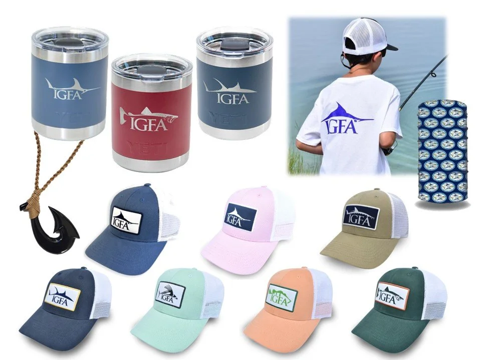 Collection of IGFA gear including insulated tumblers, printed hats in various colors, and a boy fishing wearing an IGFA t-shirt, with a fishing reel and a fishing-themed folding blanket.