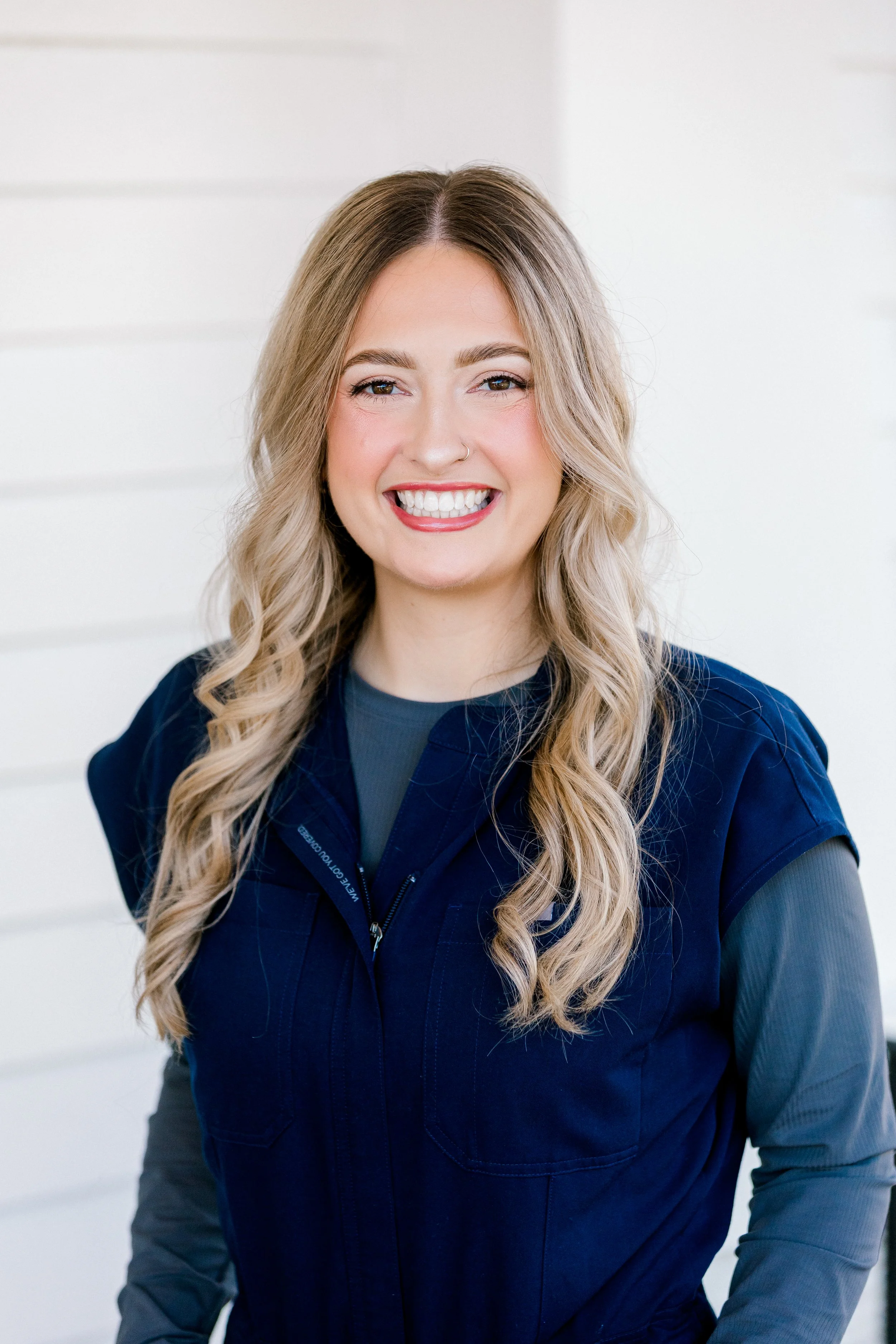 A young blonde woman wearing a blue shirt smiling outdoors.