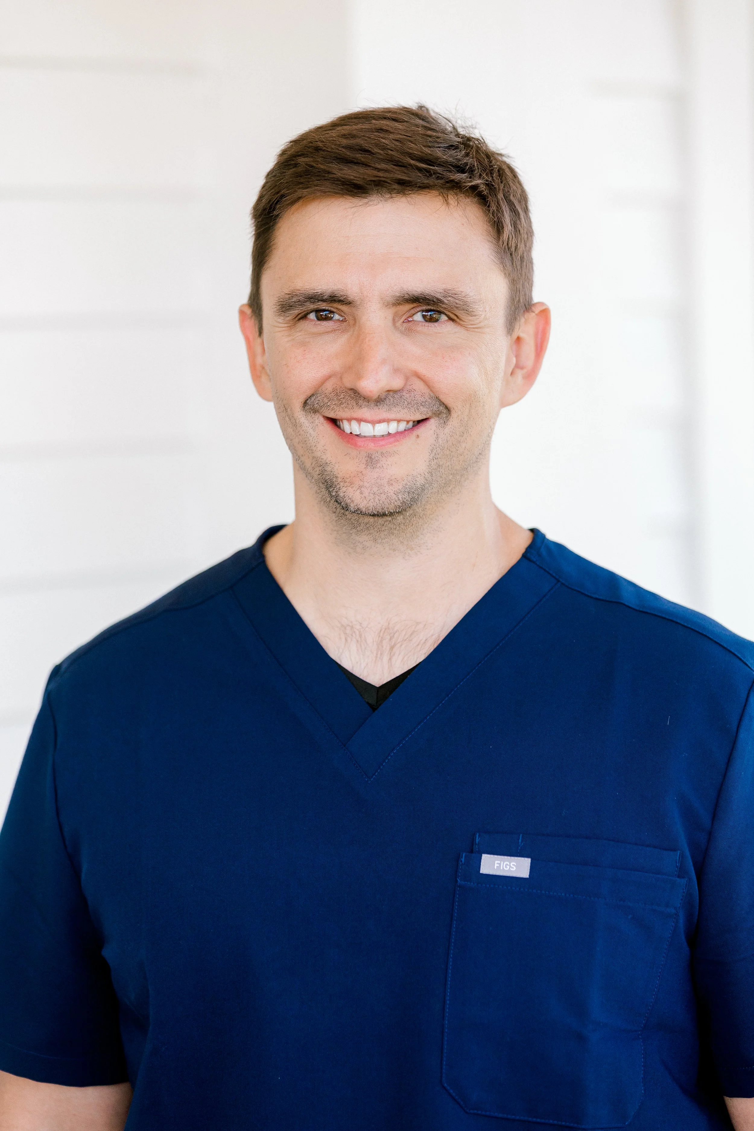 Male doctor in white coat smiling at camera with a plain white background.