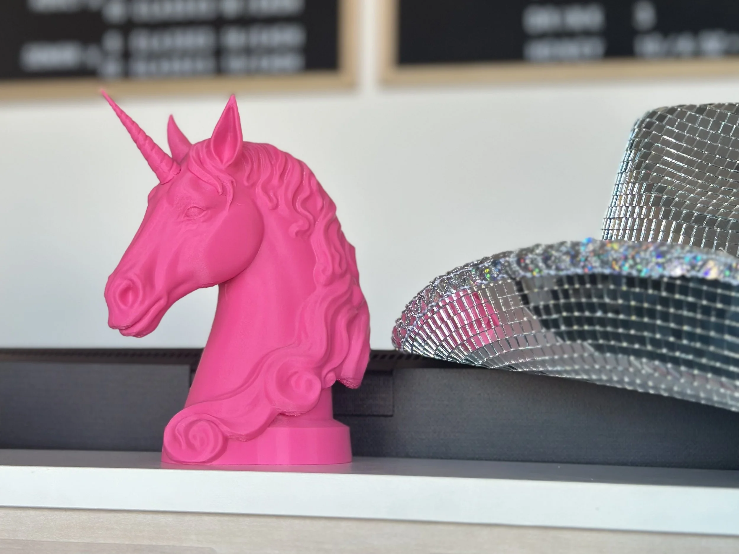 A pink 3D-printed unicorn head figurine wearing a silver disco cowboy hat