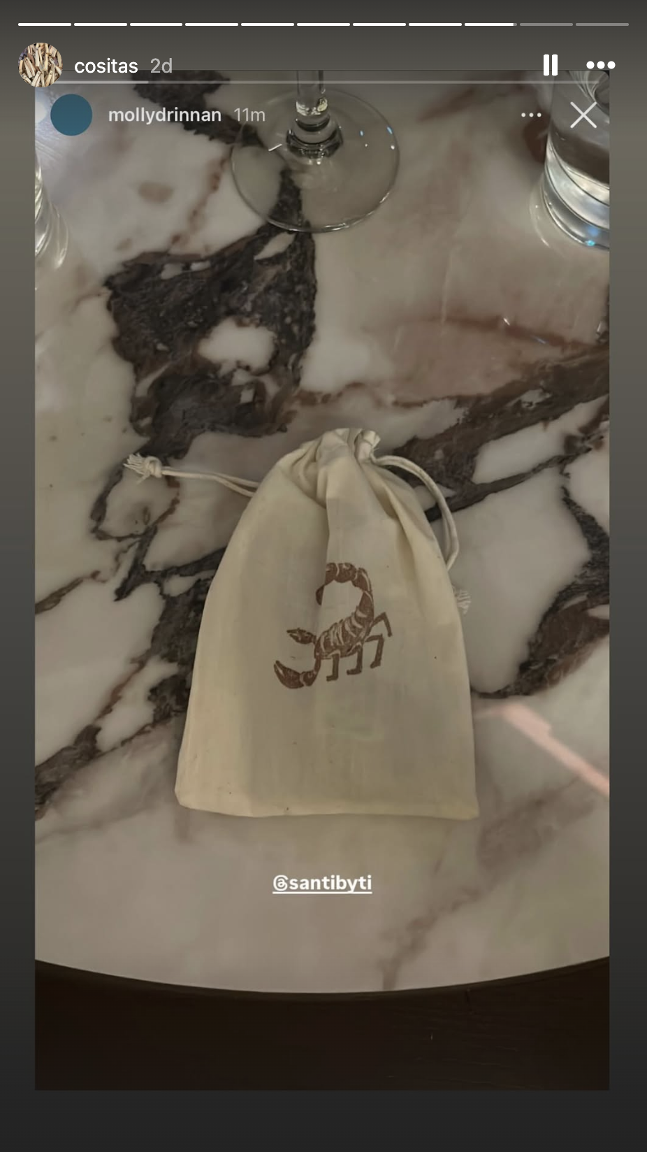 Marble table with a wine glass, a water glass, a cloth bag with a scorpion logo, and some black and white marble patterns.