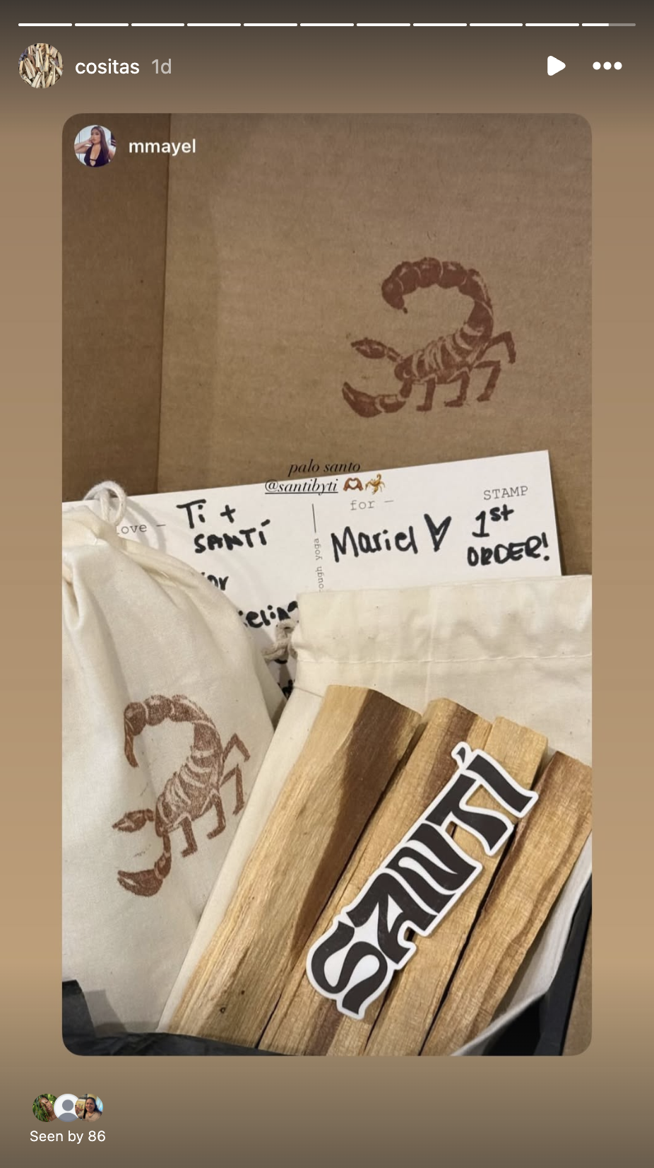 A cardboard box with a scorpion print, a white cloth bag, a white card with handwritten notes, and wooden pieces with a sticker that says 'SAI'.