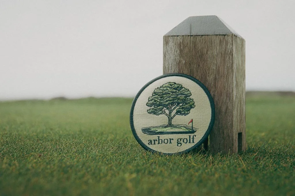 Golf course marker with "arbor golf" patch featuring a tree and flag.