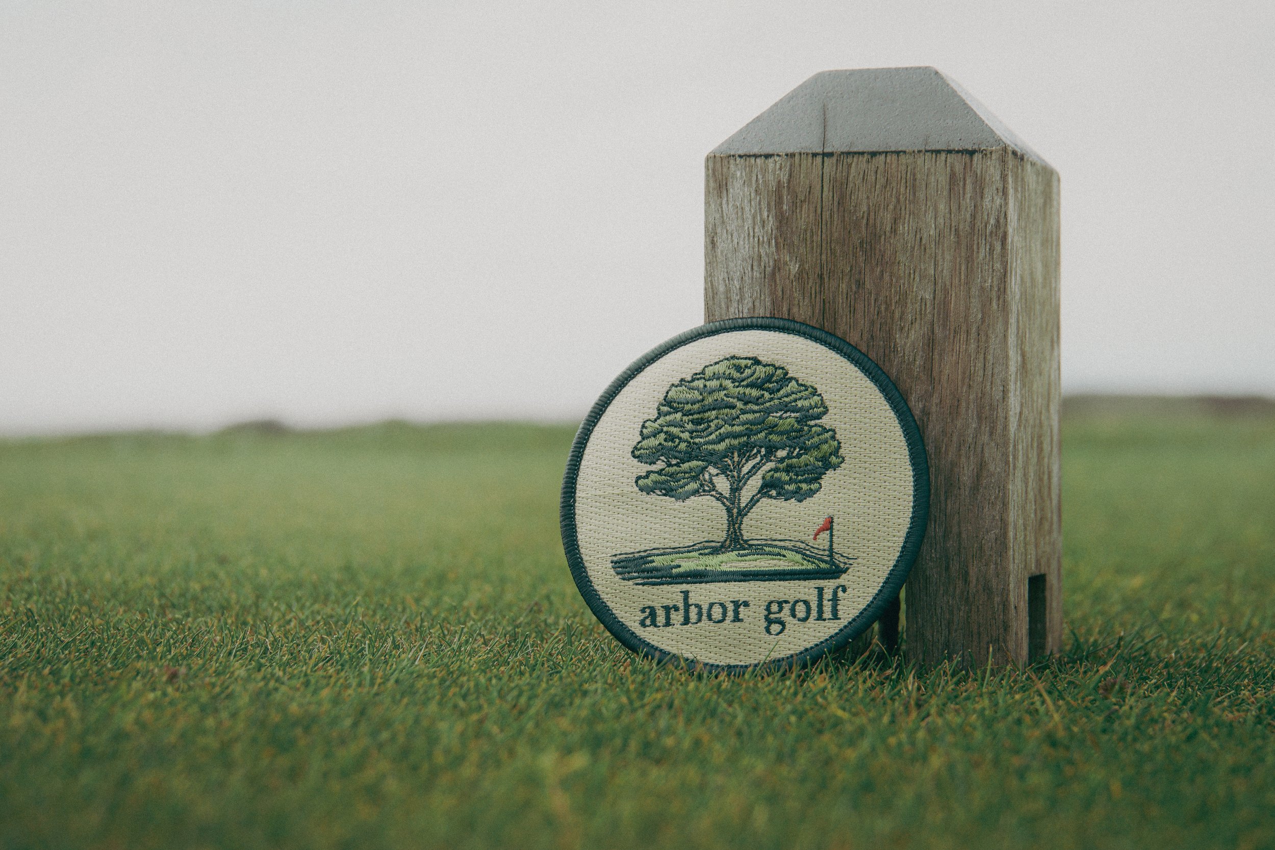 Golf course sign with "arbor golf" patch featuring a tree and flag on grassy field.