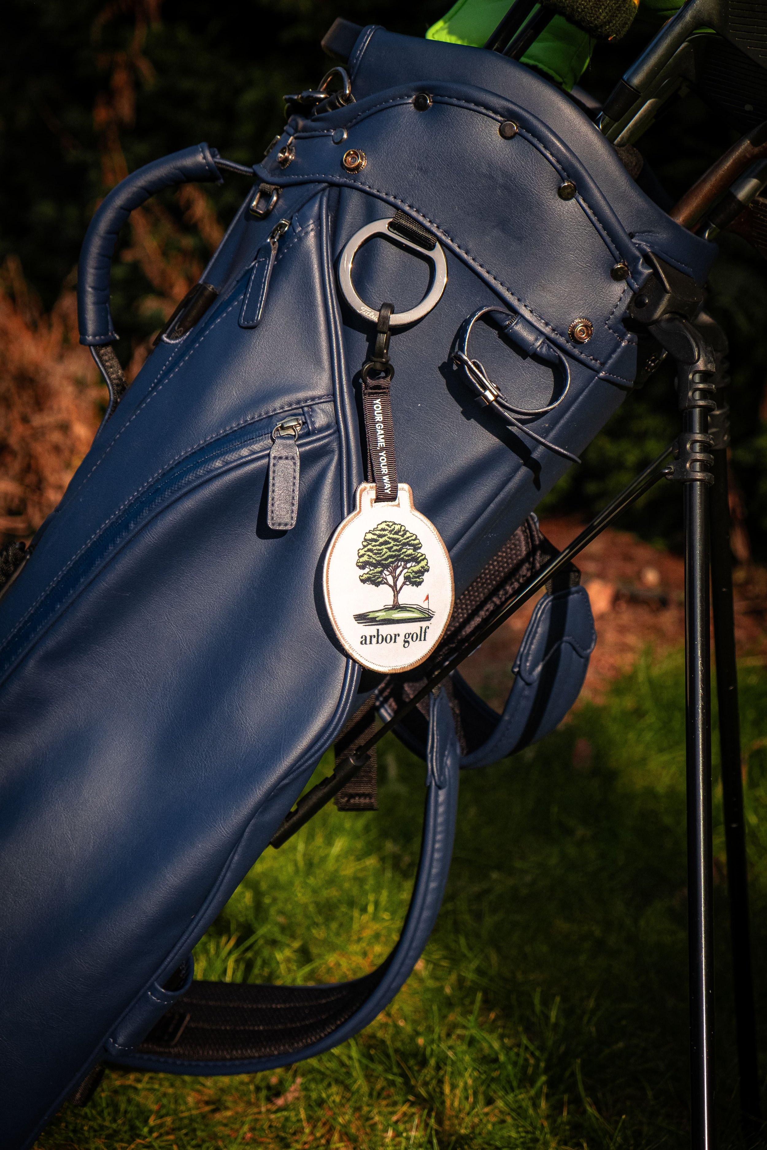 Blue golf bag with a "arbor golf" tag attached, placed on grass.