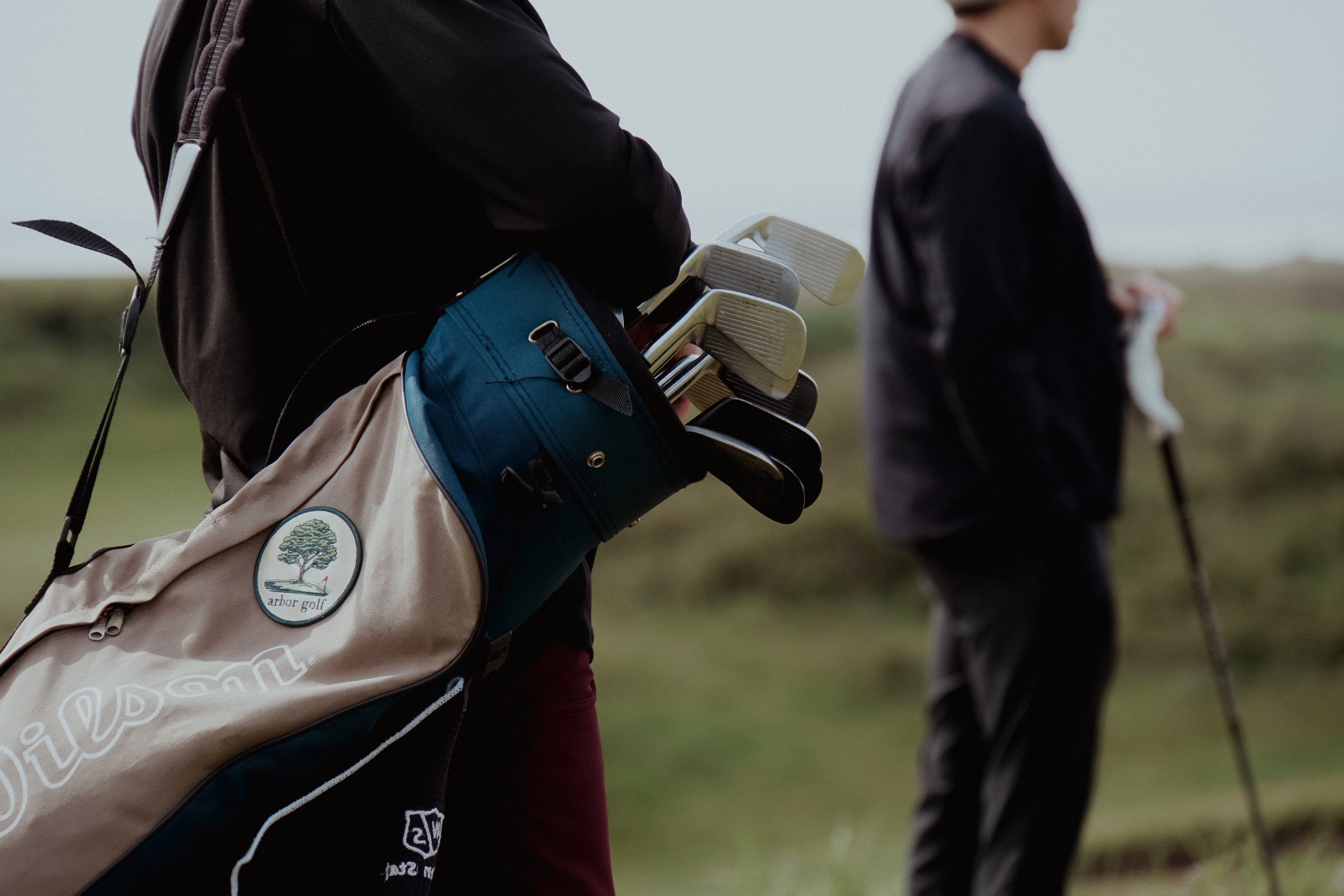 Person carrying a golf bag with clubs on a golf course.