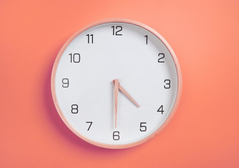 A round, white clock with the numbers 1-12 on a coral colored wall.