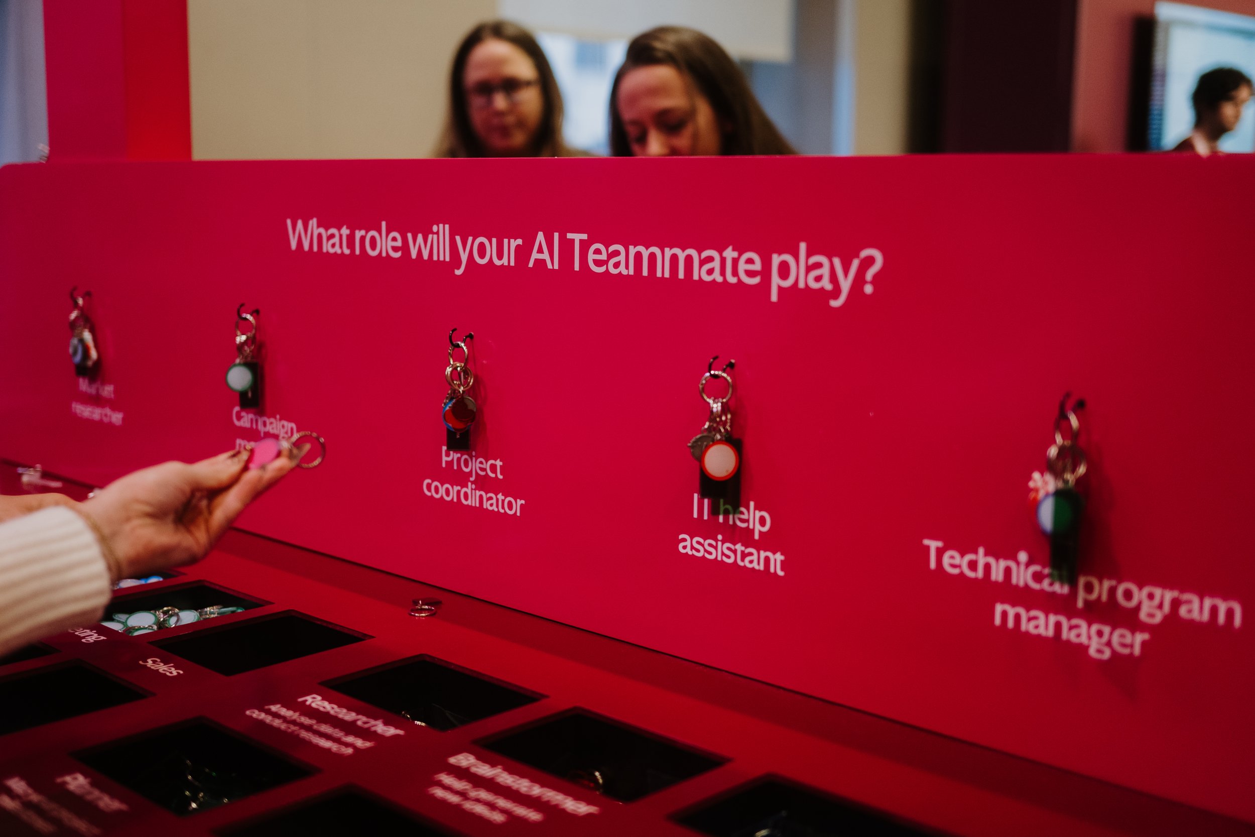 An image taken at Asana's 2025 Work Innovation Summit, a red display that reads "What role will your AI Teammate play?" with hanging keychains above multiple potential AI use options