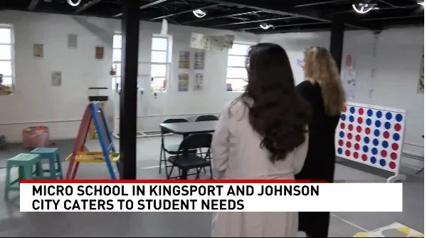 Two women in a classroom or activity room with a Connect Four game, colorful stools, and a ladder, engaged in conversation. The caption reads 'Micro School in Kingsport and Johnson City caters to student needs.'