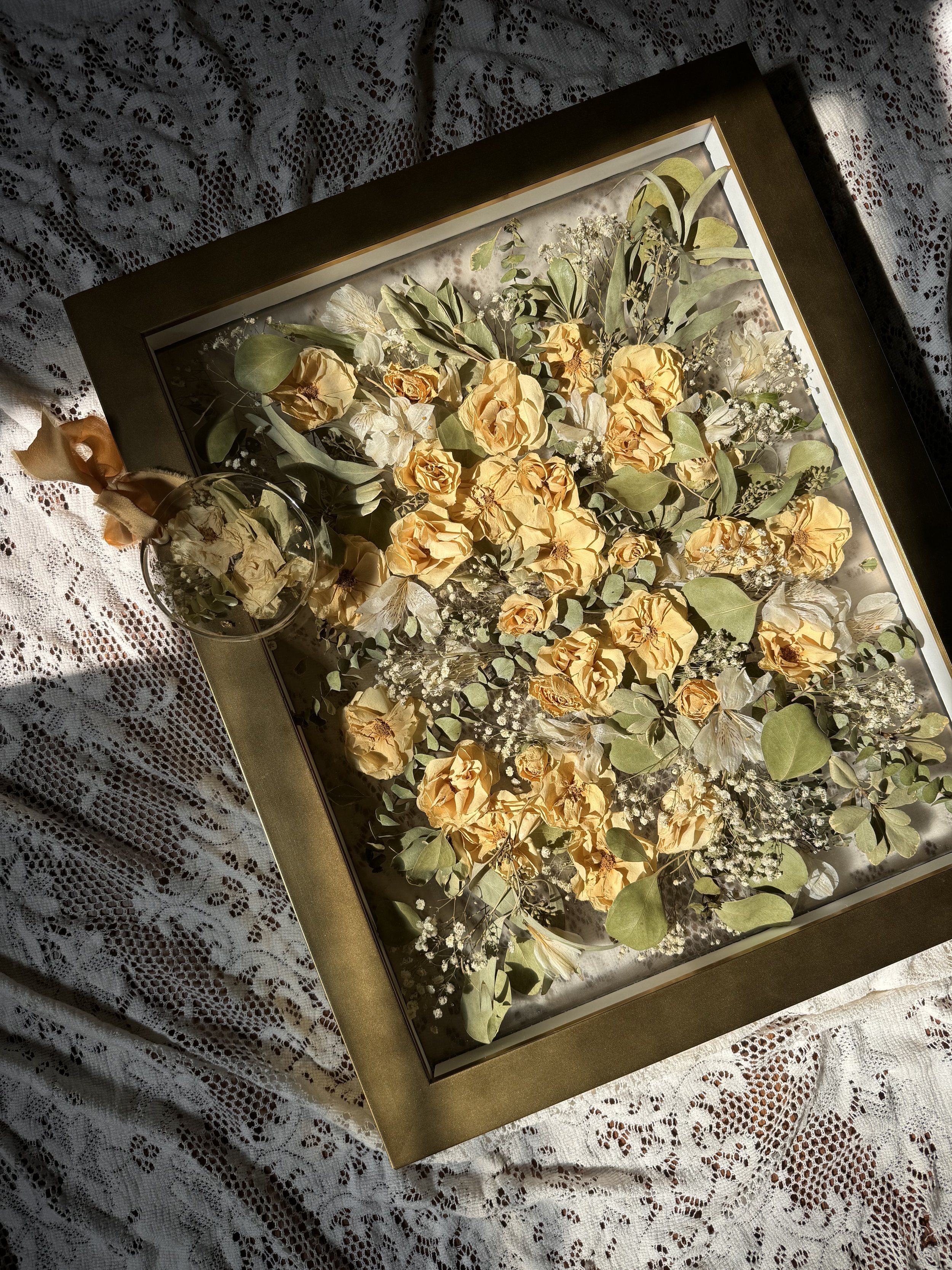 Framed arrangement of dried yellow roses and greenery on lace fabric