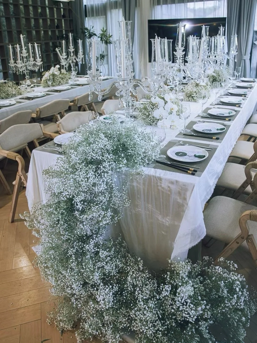 Elegant wedding table setup with white floral arrangements, glass candelabras, and place settings on a long white table.