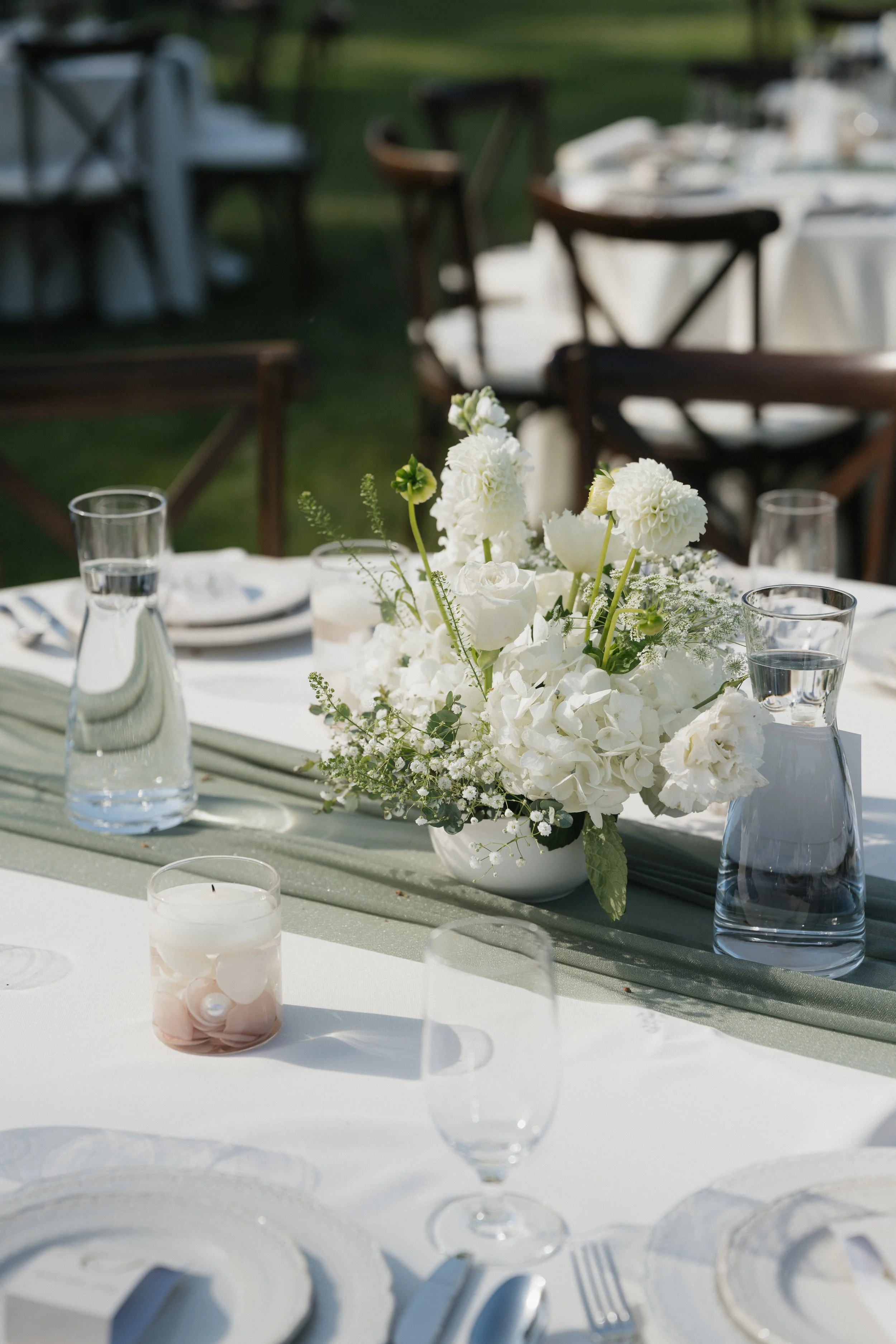 Elegant outdoor dining table with white floral centerpiece, glassware, and neatly arranged place settings.