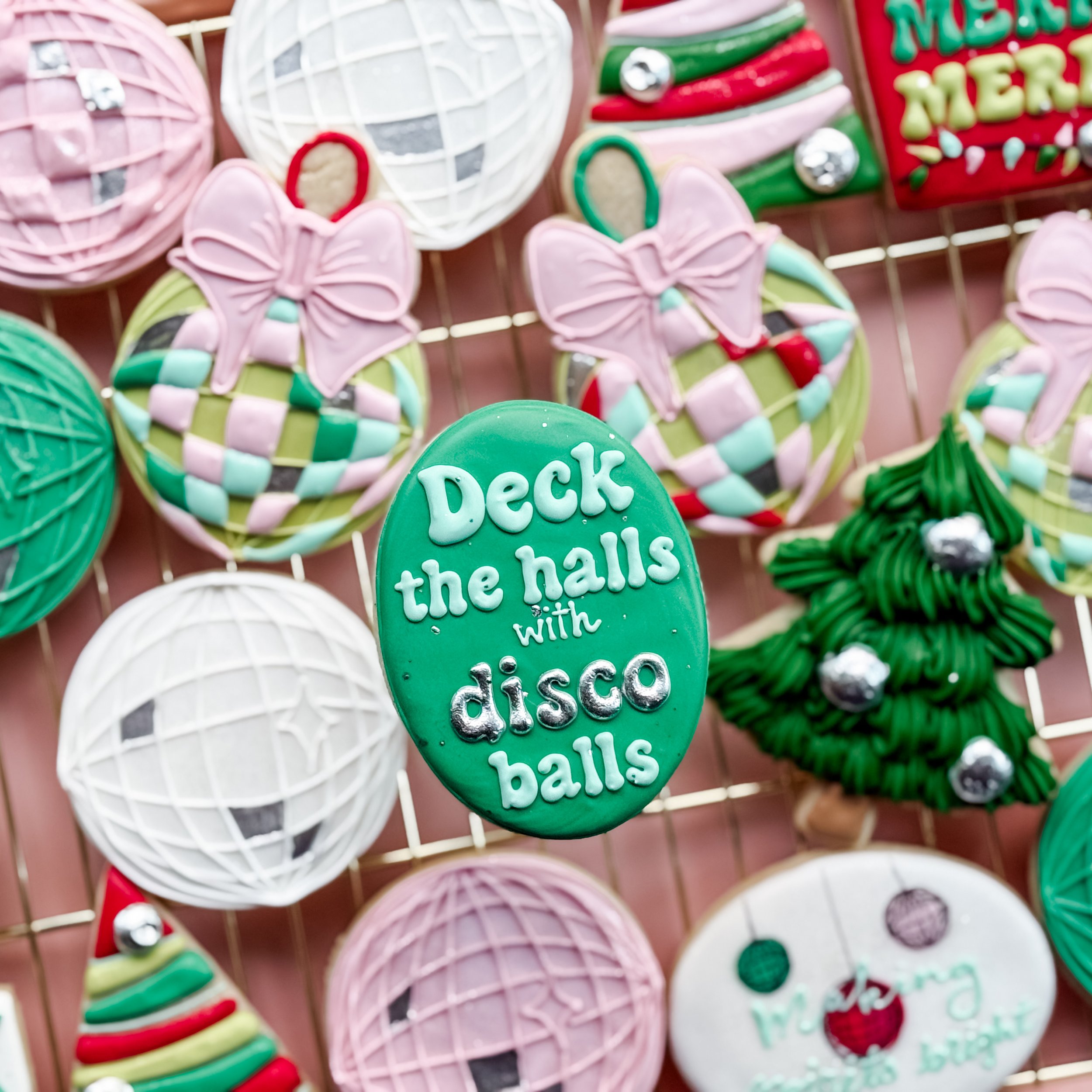 Decorative holiday cookies including pink butterfly cookies with bows, spherical ornaments, and decorated cookies with Christmas themes displayed on a wire rack.