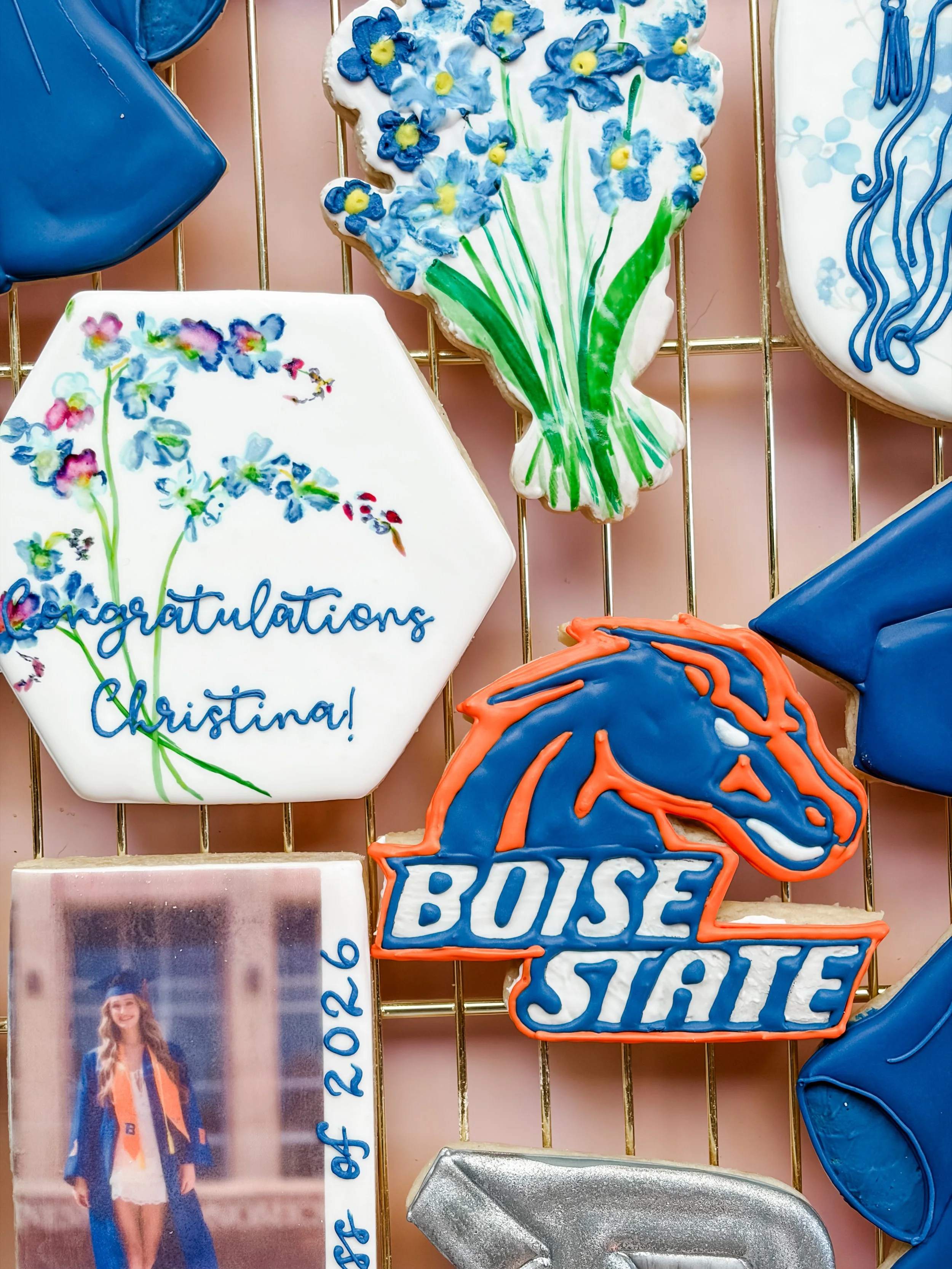 Decorative cookies shaped and decorated with flowers, a 'Congratulations' message, a state shape with 'BSU' written, and a person in graduation attire.